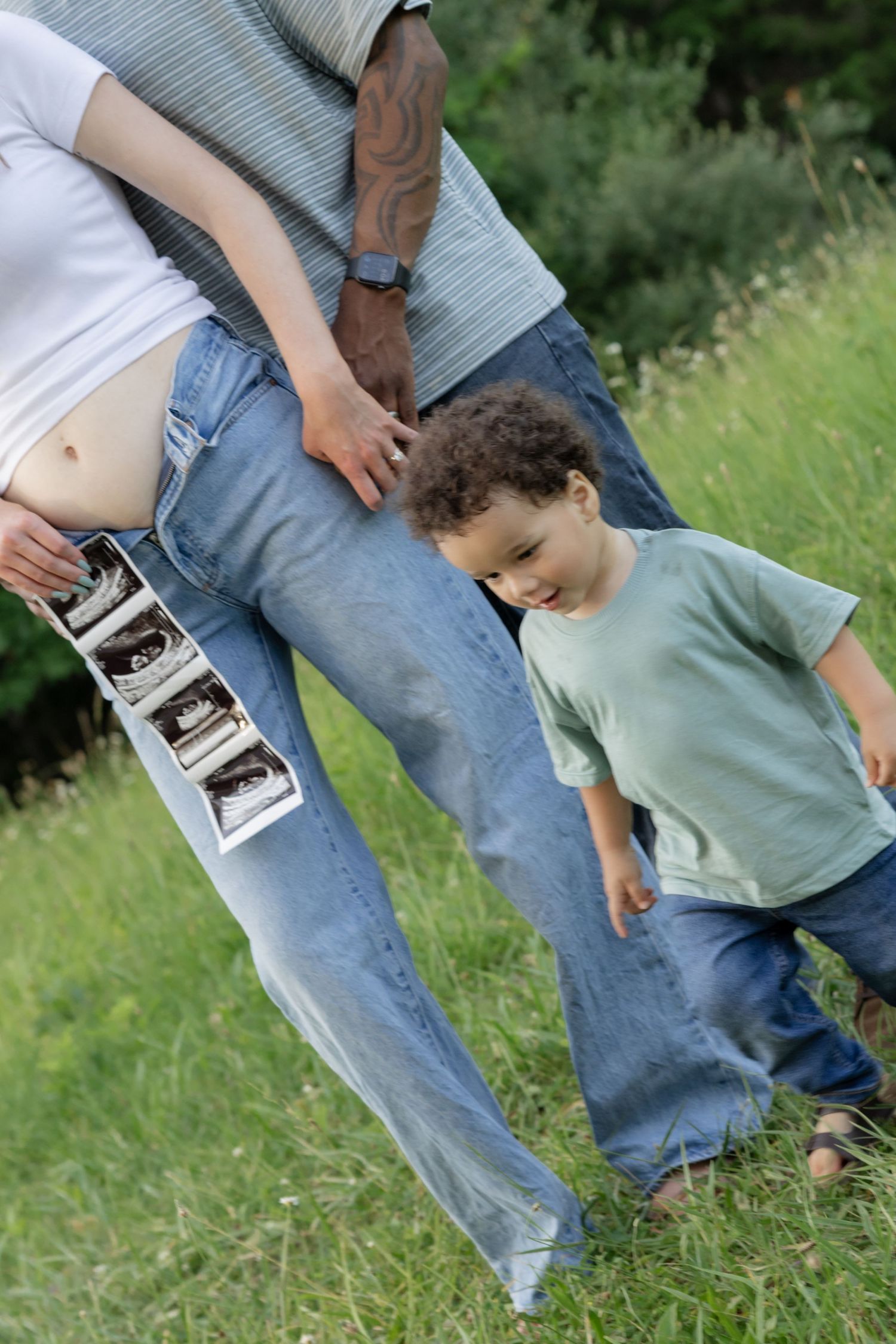 A couple holding ultrasound photos in a grassy field during a pregnancy announcement.