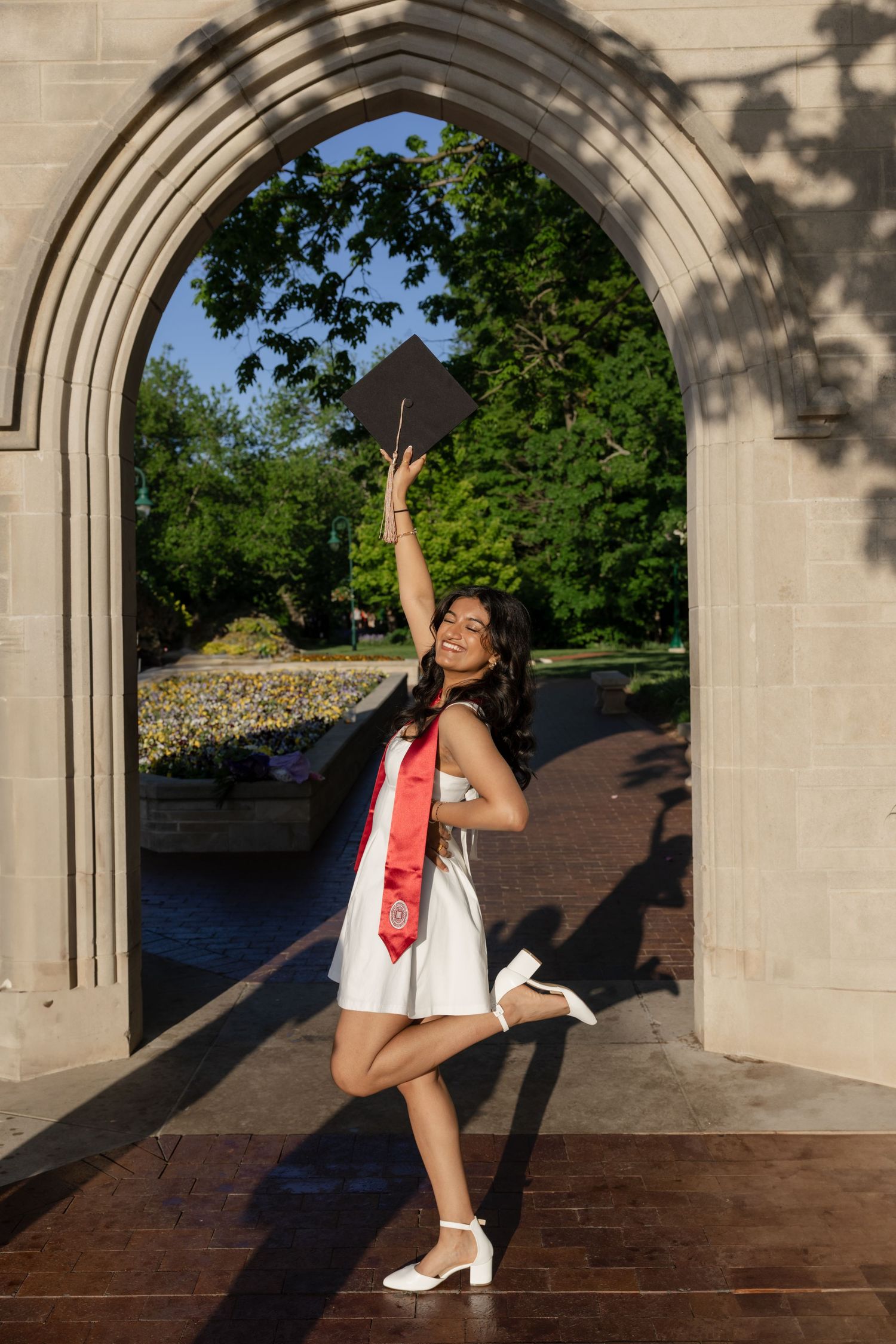 Someone in a white dress with red sash poses dramatically under a stone archway.