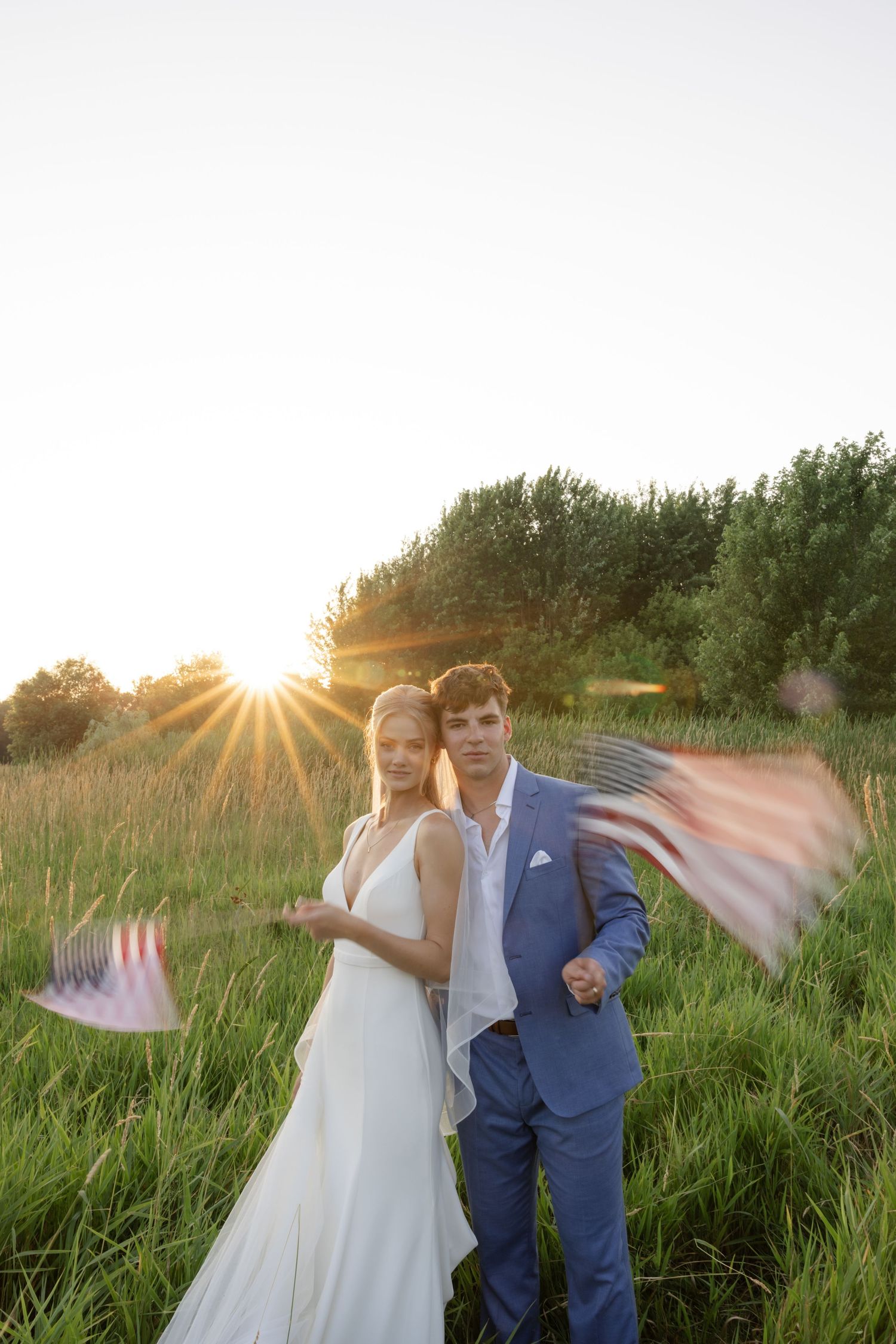 Newlyweds playfully posing in field during sunset with flowing veil.