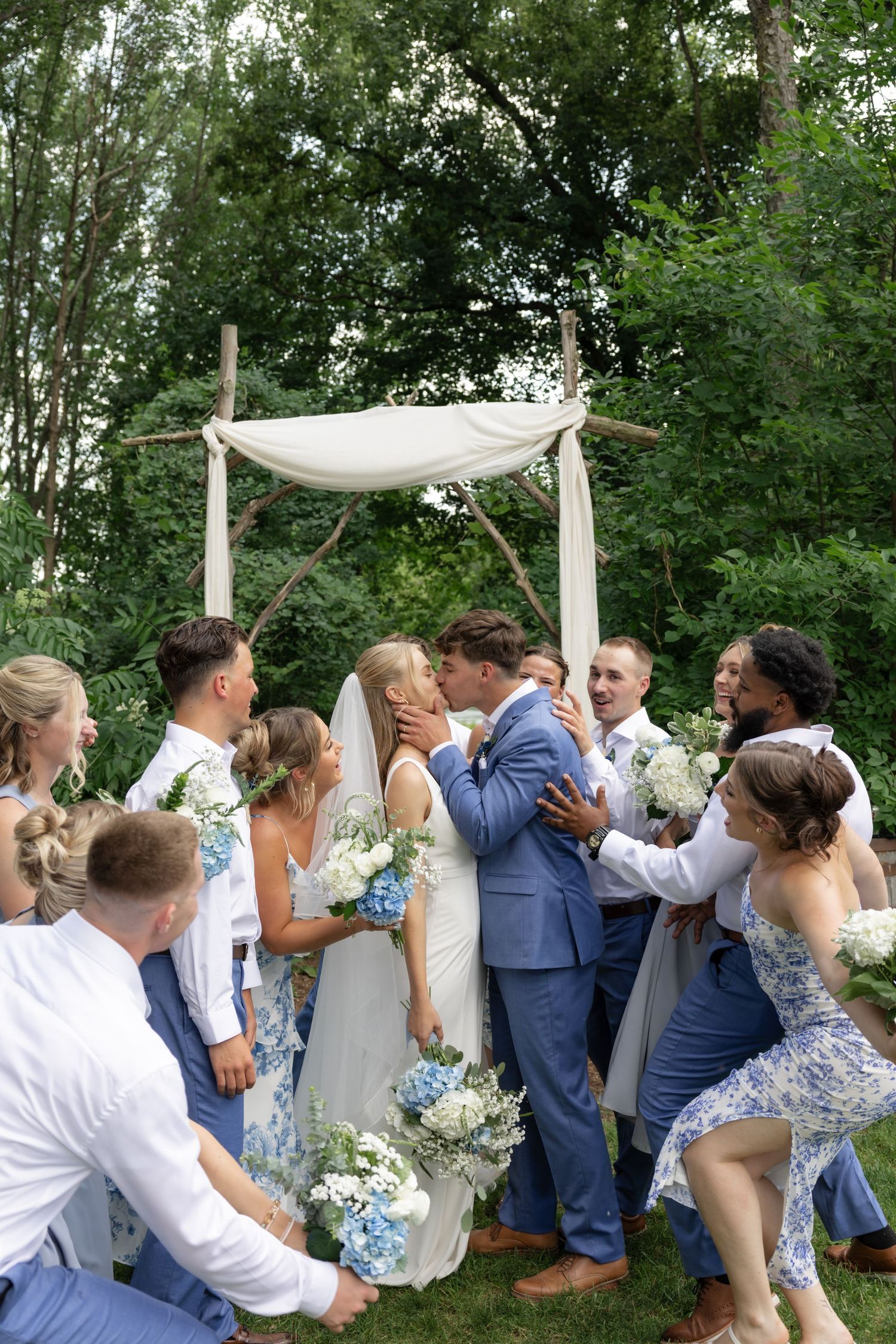 Candid moments of wedding party celebrating and embracing under white fabric ceremony backdrop.