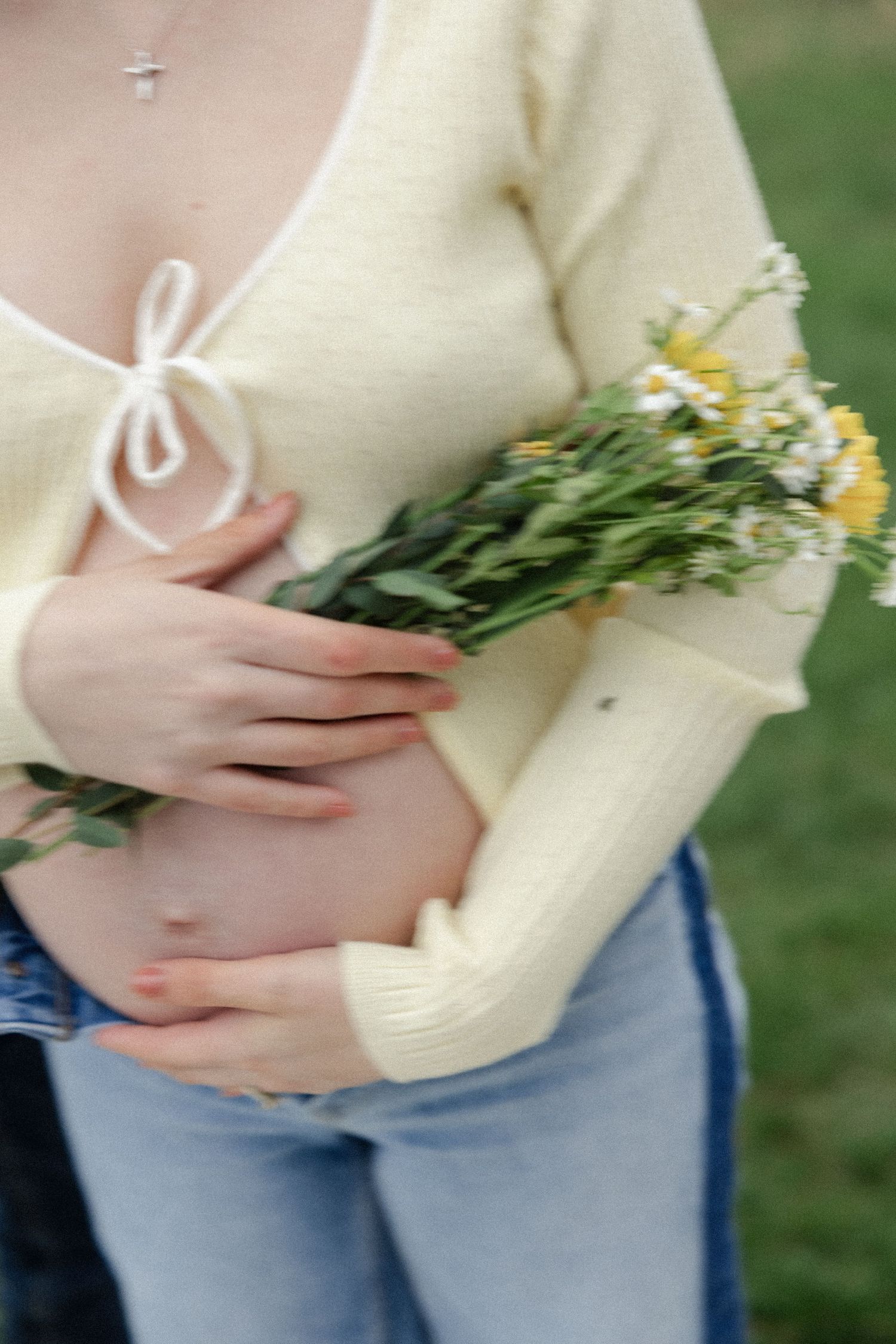 Close up of pregnant belly with yellow wildflowers and cream sweater.