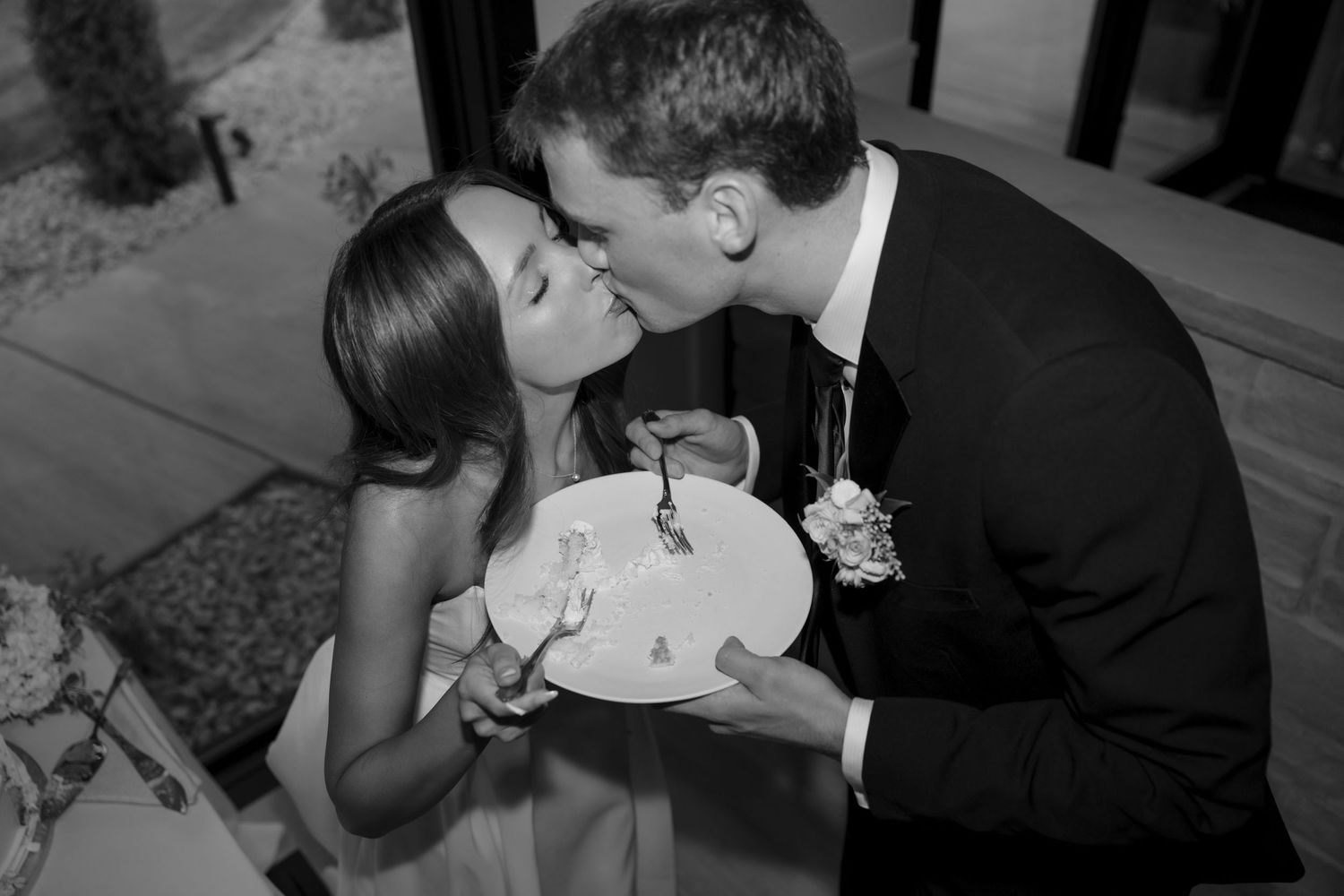 Newlywed couple shares a romantic cake cutting kiss at their wedding reception.