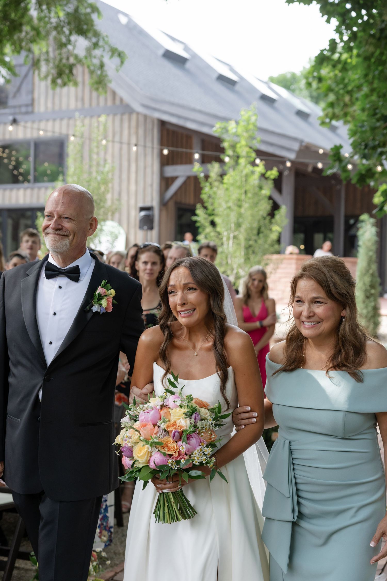 Bridal party walks outdoors with bride holding colorful bouquet in white gown.