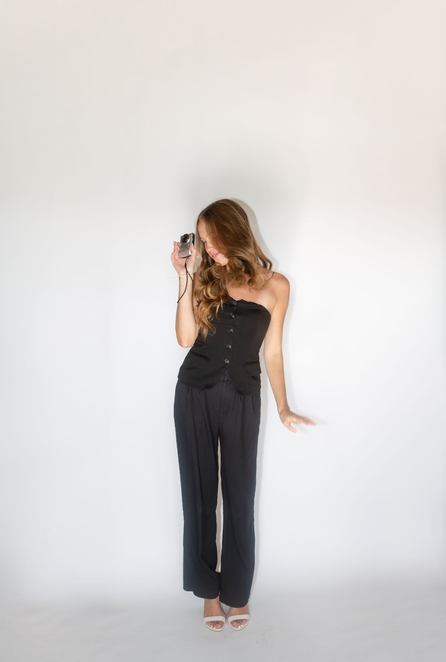 Photographer in black strapless outfit focuses through vintage camera lens in studio setting.