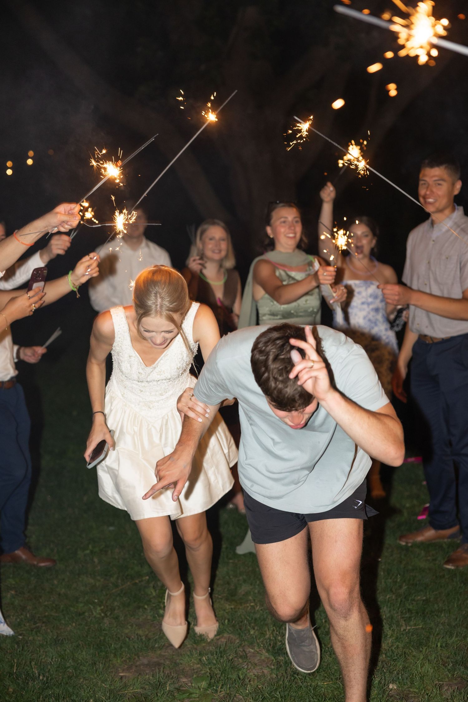 Celebratory group poses with sparklers on a grassy lawn at night.