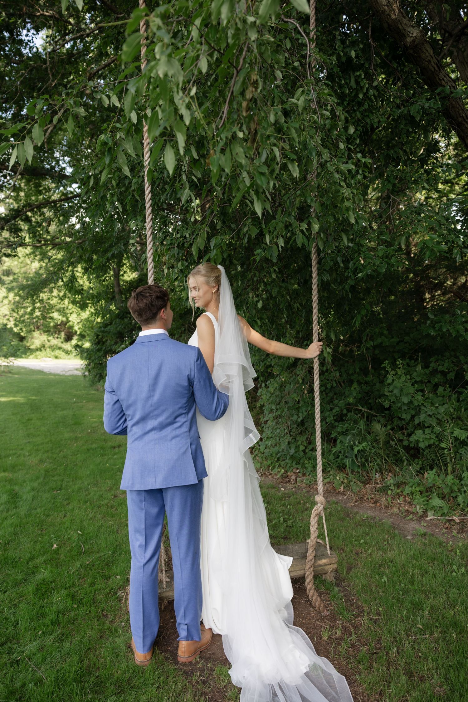 A couple in blue suit and white wedding dress walking through a lush garden path.