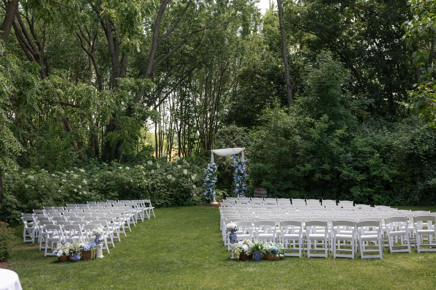 Panoramic view of white wedding ceremony chairs set up in a garden setting.