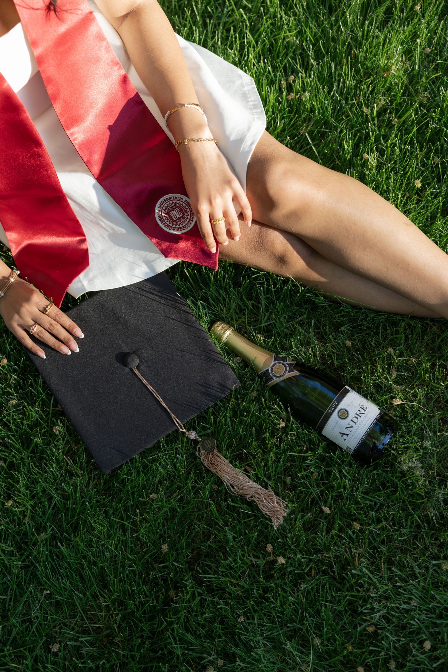 Someone relaxing on green grass with wine and snacks laid out for a picnic.