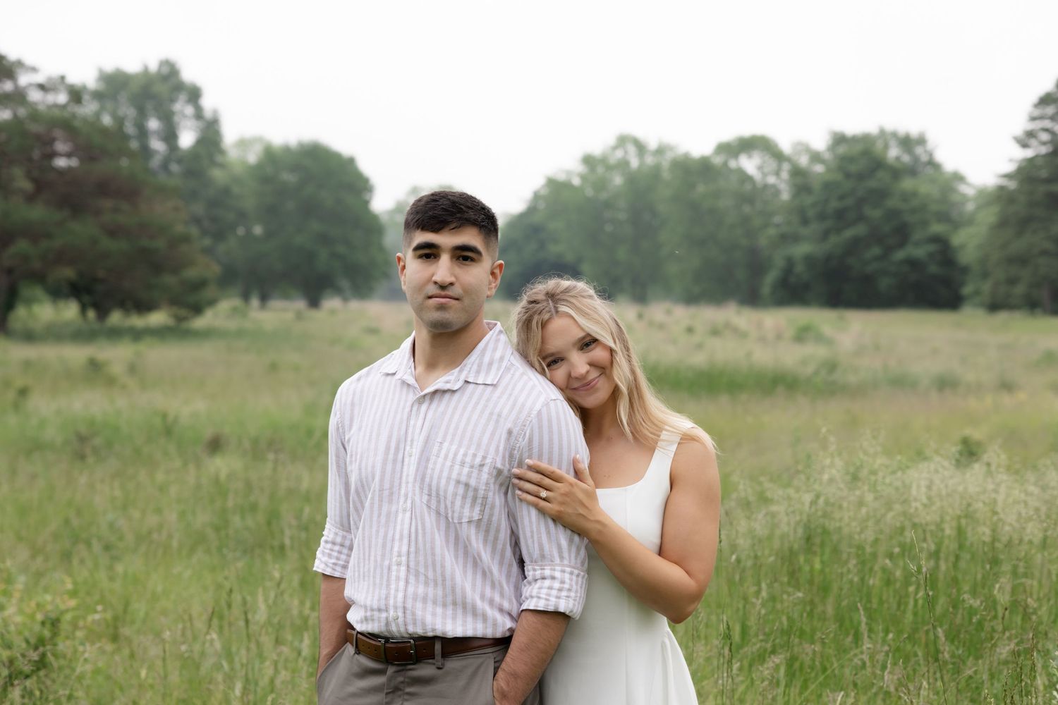 Two people embrace in a romantic moment while standing in a summer field.