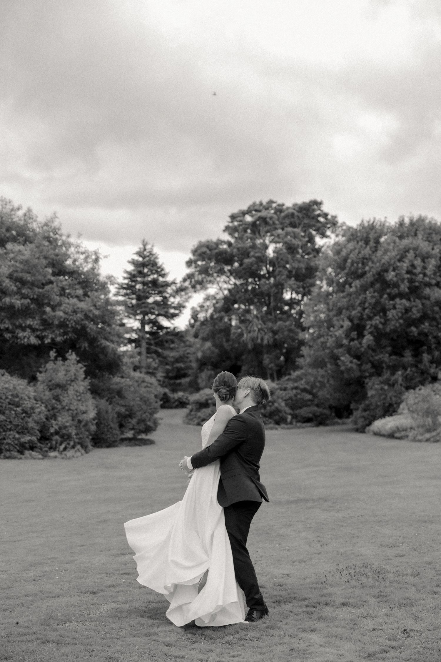 Black and white wedding photo of dancing couple in garden setting.