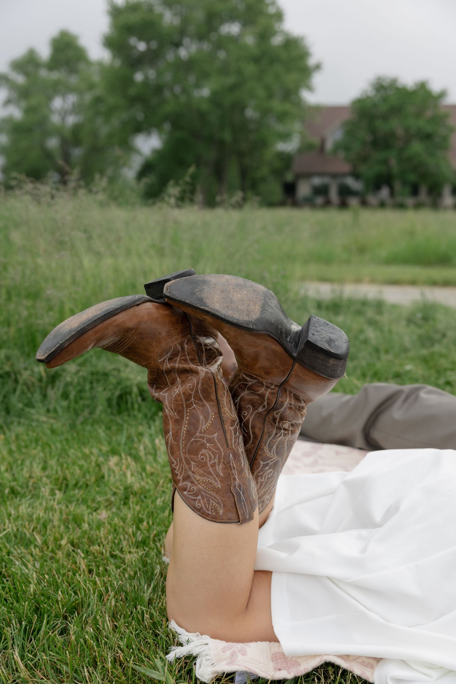 Brown boots lay in green grass next to flowing white fabric.