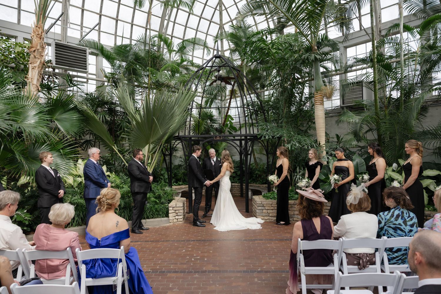 Wedding ceremony in a glass conservatory filled with tropical plants.