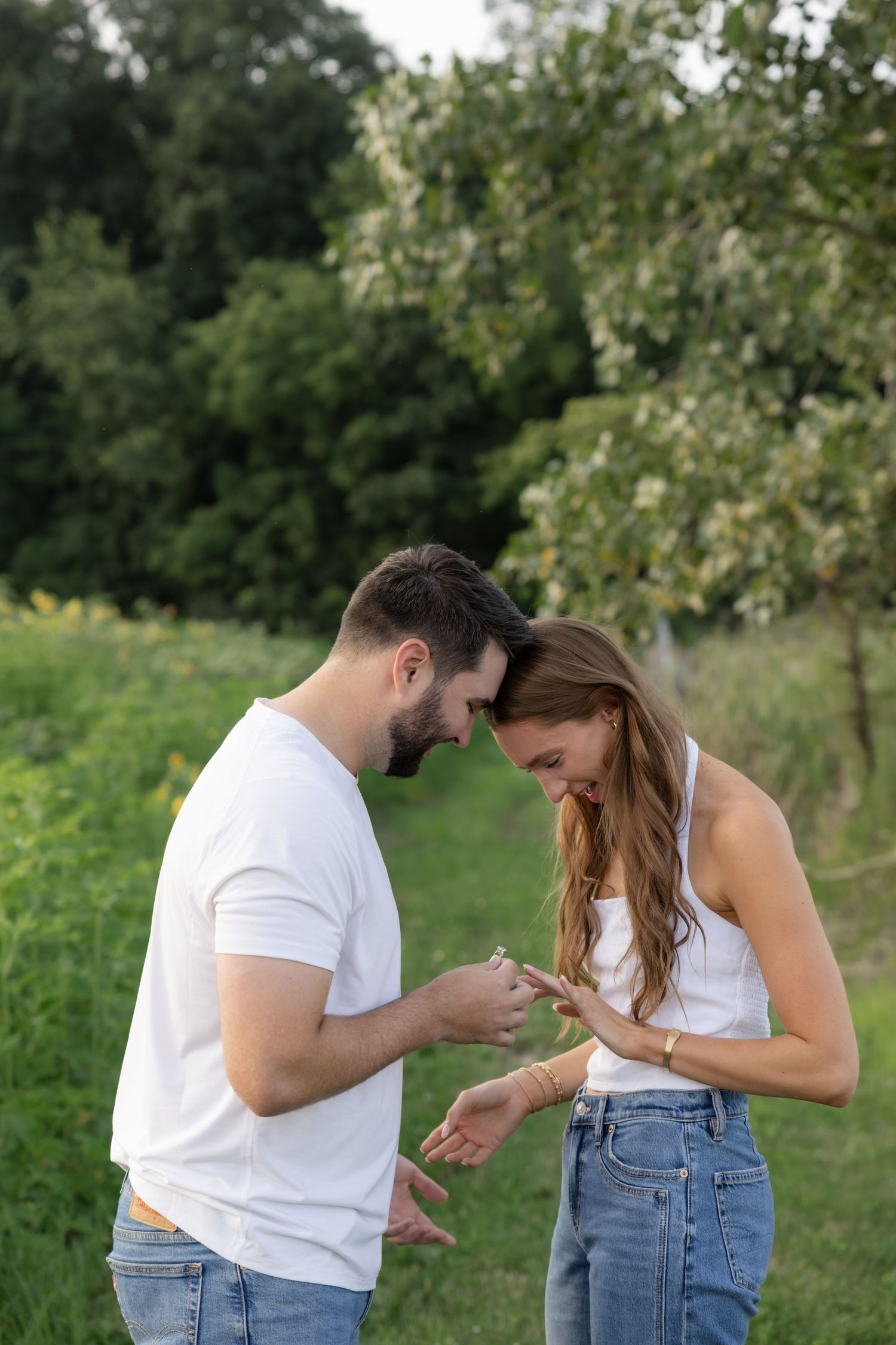 A couple in white shirts and jeans sharing a sweet moment together in a sunny outdoor field.