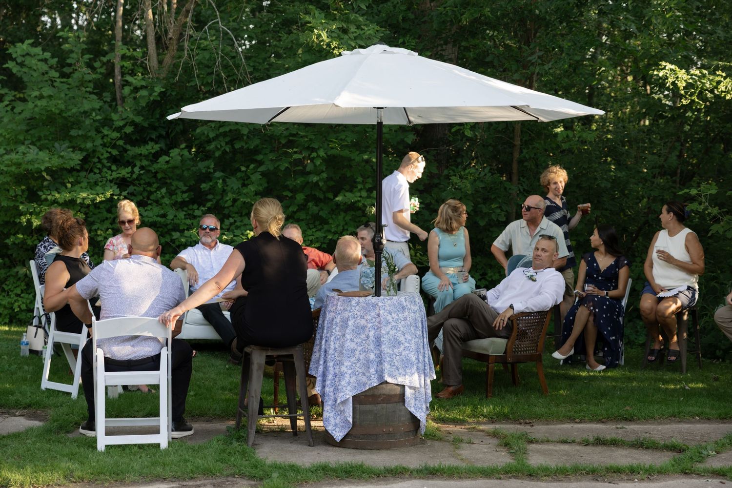 Wedding guests relax under white umbrellas at outdoor tables during a casual reception.