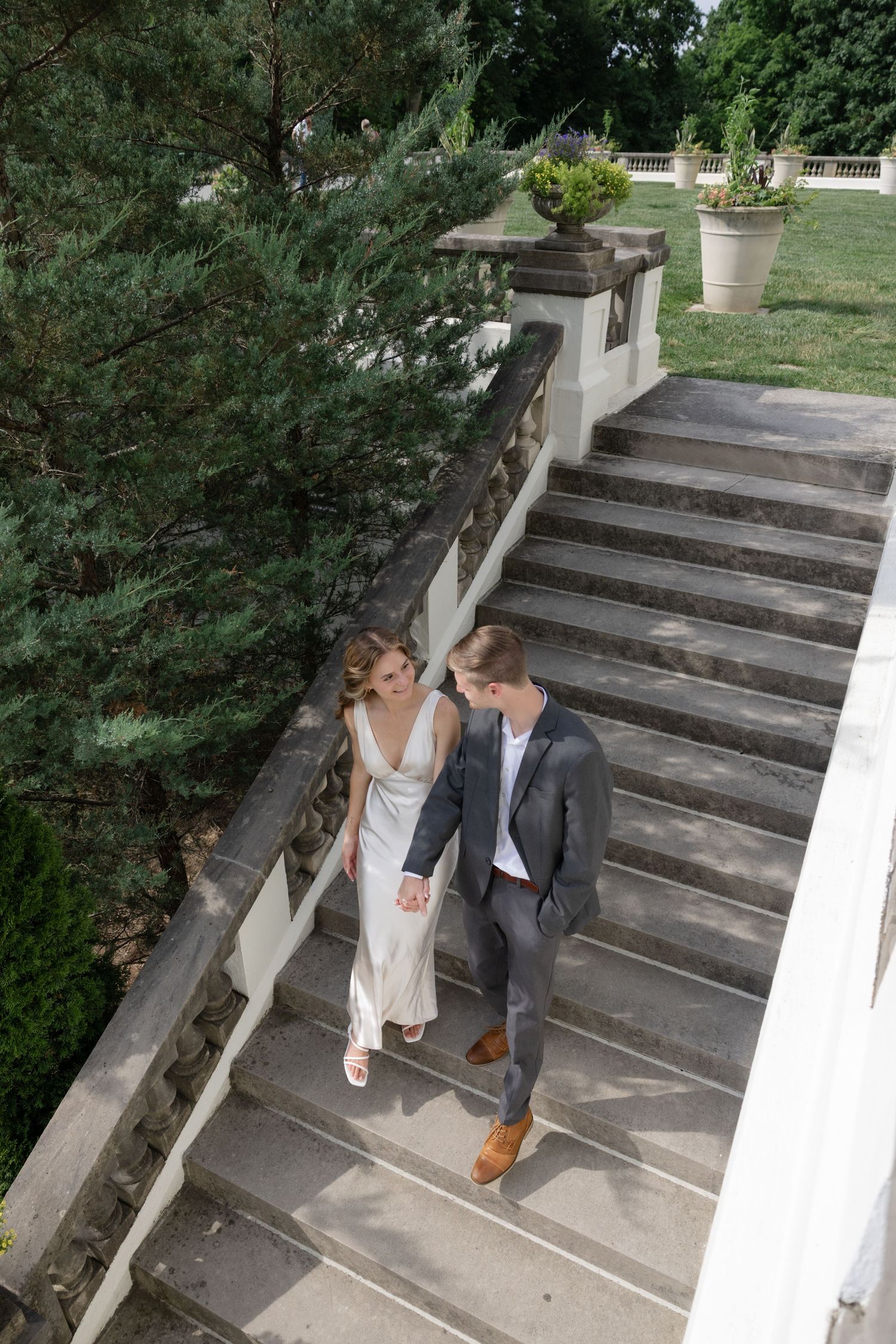 Elegant couple descends stone steps together at historic mansion.