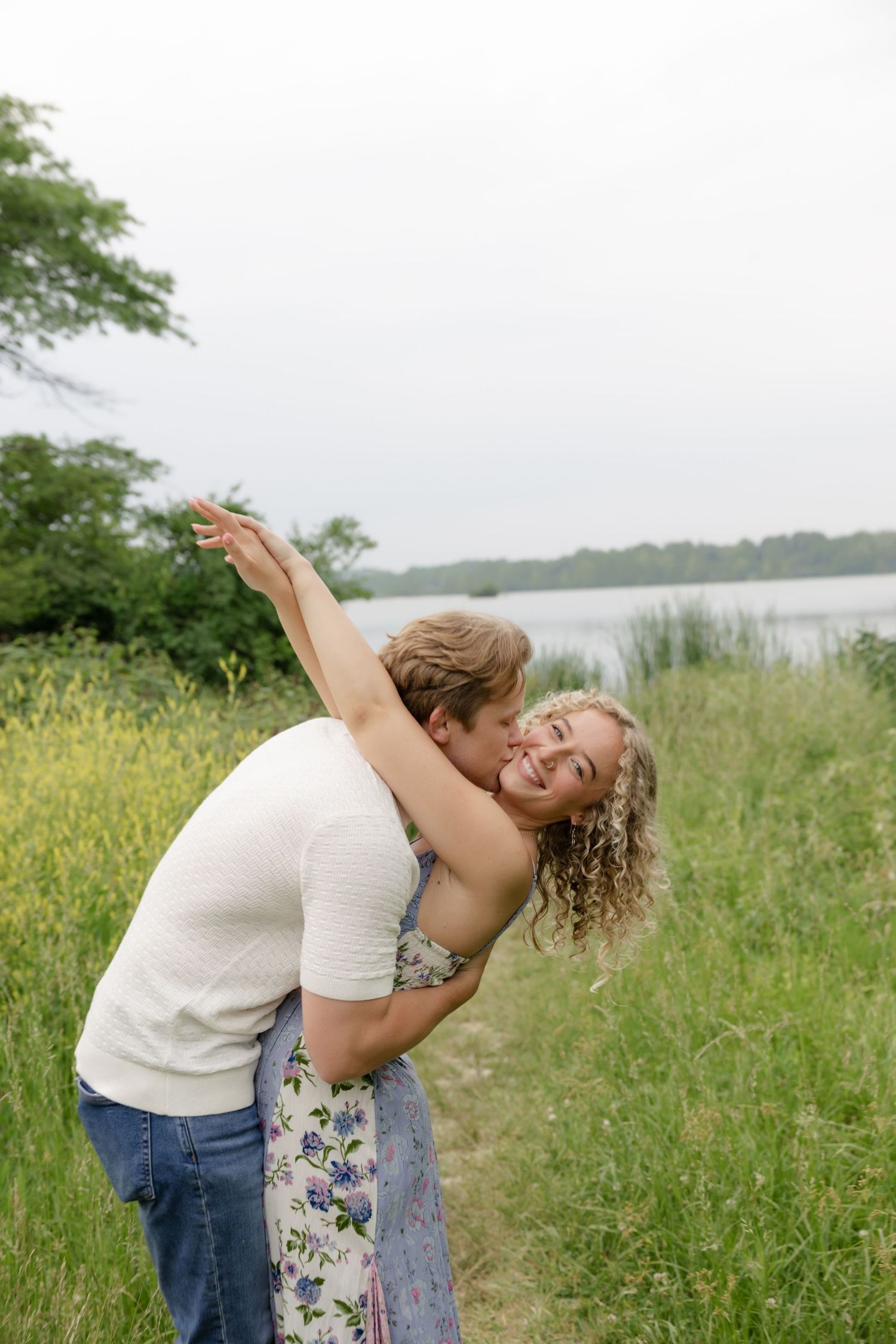 Playful couple sharing joyful moments and dancing in a meadow by the water.