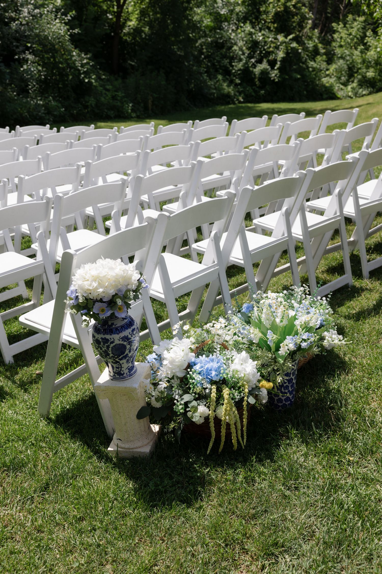 White folding chairs with floral decorations arranged for outdoor wedding ceremony.