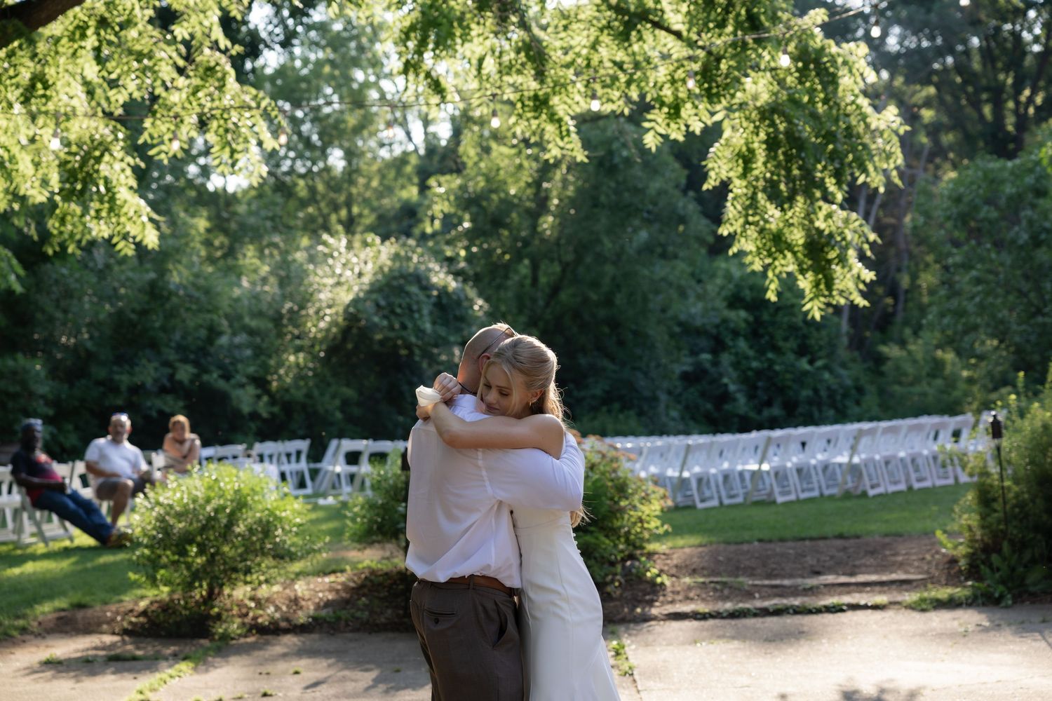 A loving embrace captured in a sunlit garden setting with white chairs in the background.