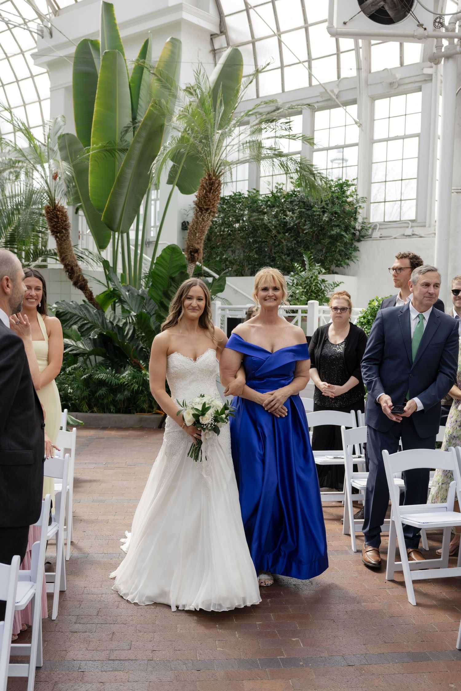 Wedding ceremony in a bright conservatory with tropical plants and elegant white decor.