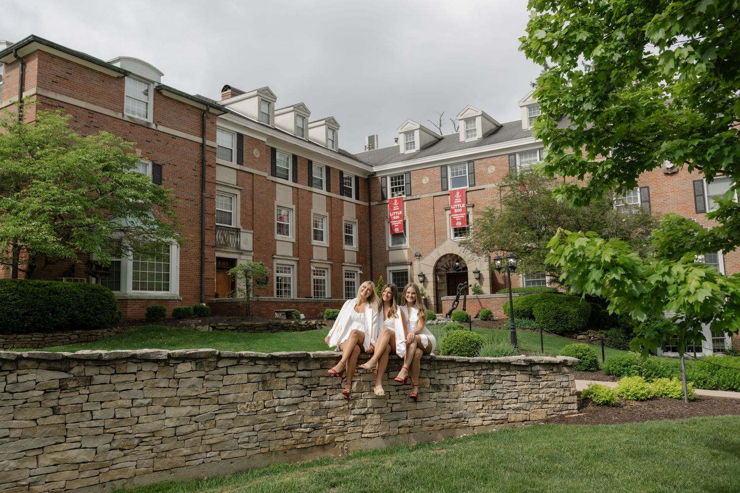 Traditional brick collegiate buildings with landscaped grounds surrounded by stone walls and greenery.