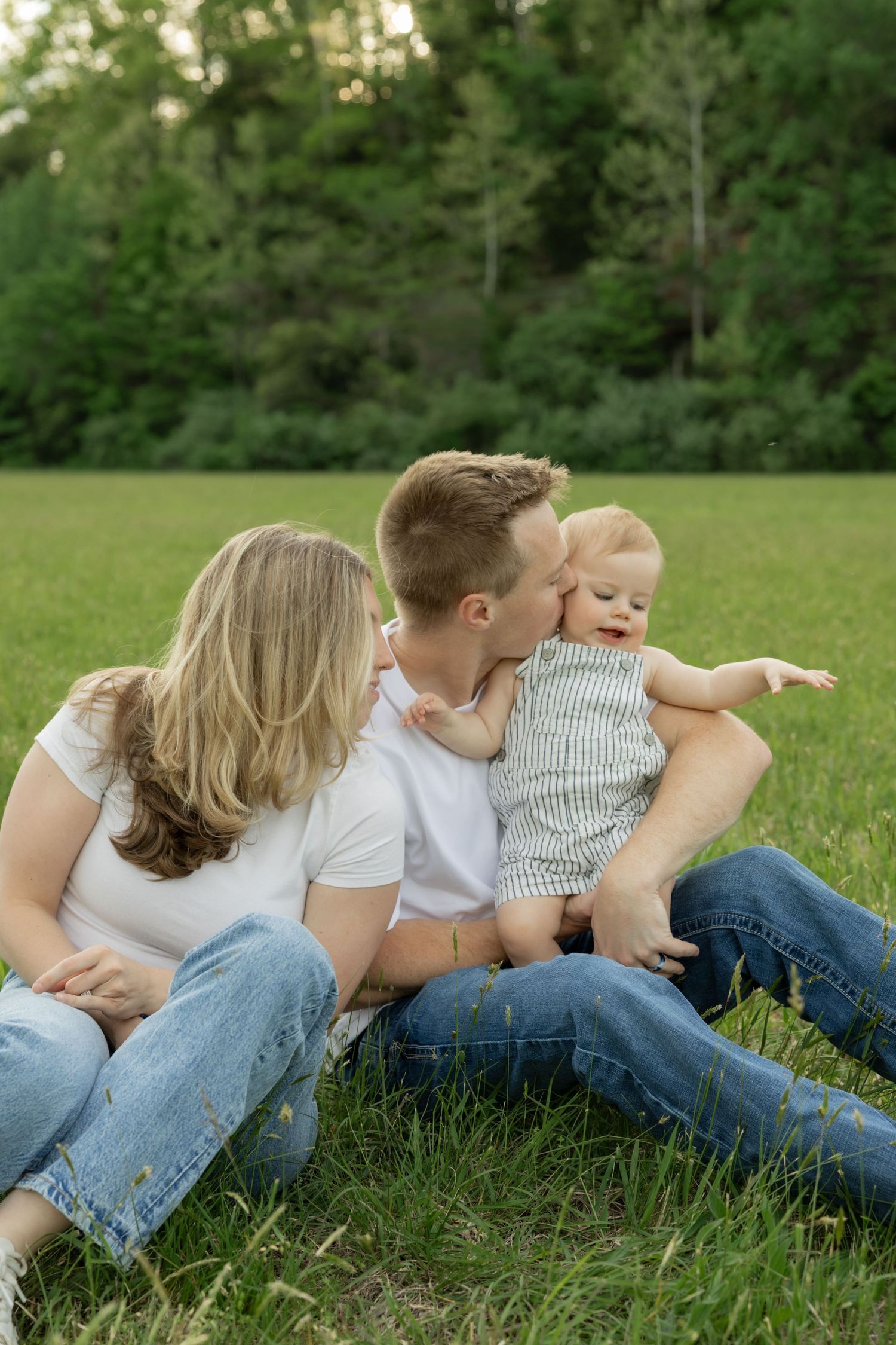 A family lies together on green grass during a casual outdoor photo session.
