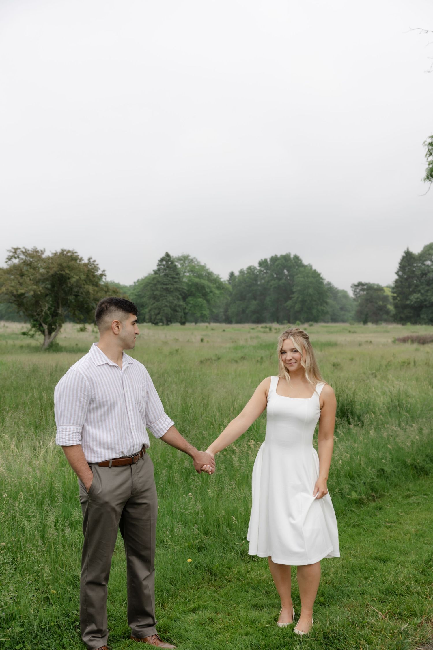 A couple playfully interacting in a green meadow on an overcast day.