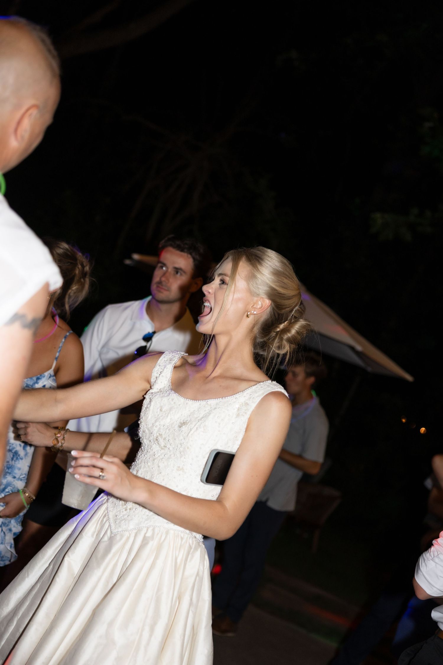 People dancing and swaying at a nighttime celebration with decorative lighting.