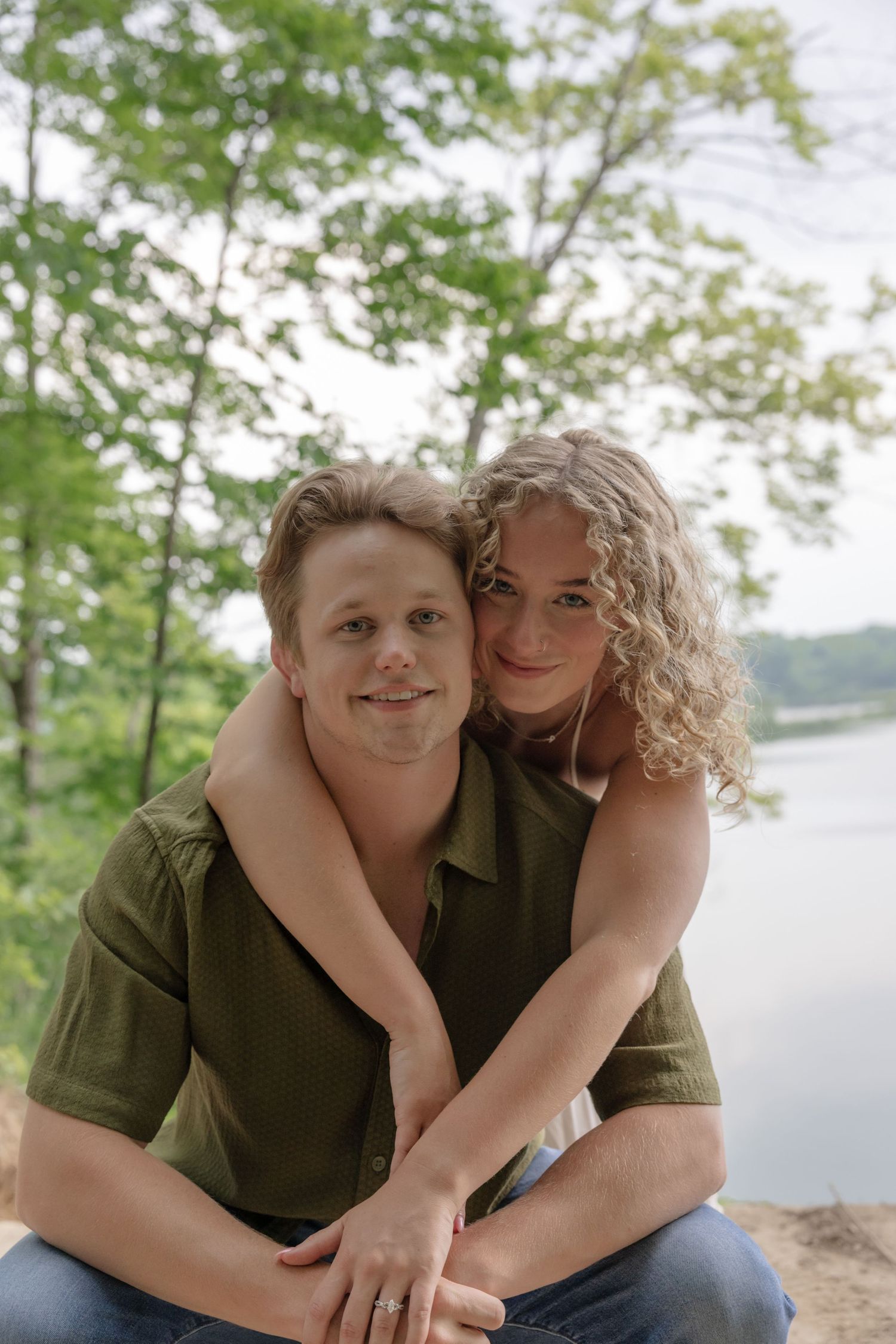 A couple shares a sweet moment together on a cliff overlooking a lake.