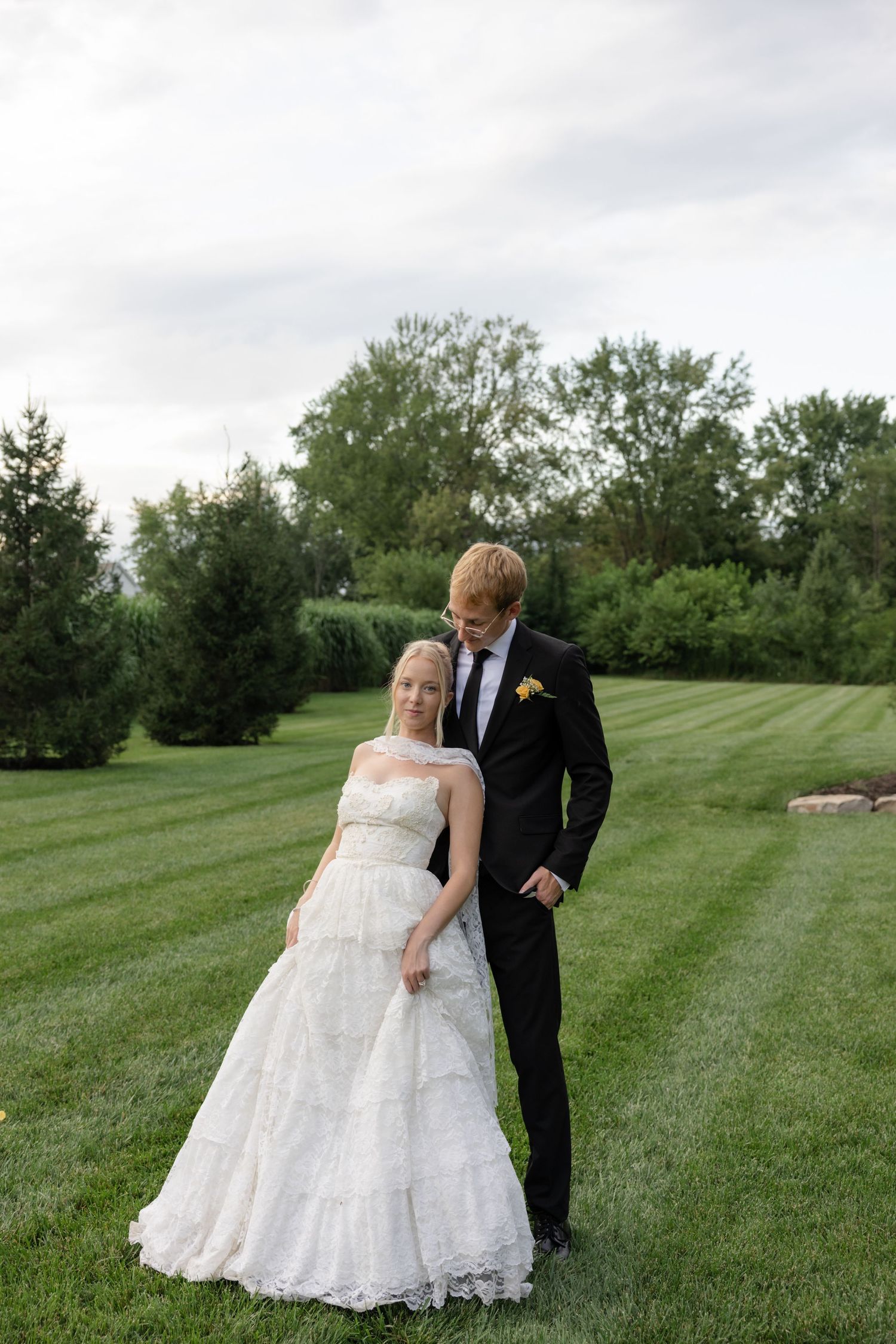 A couple poses together on lush green grass during their wedding day.