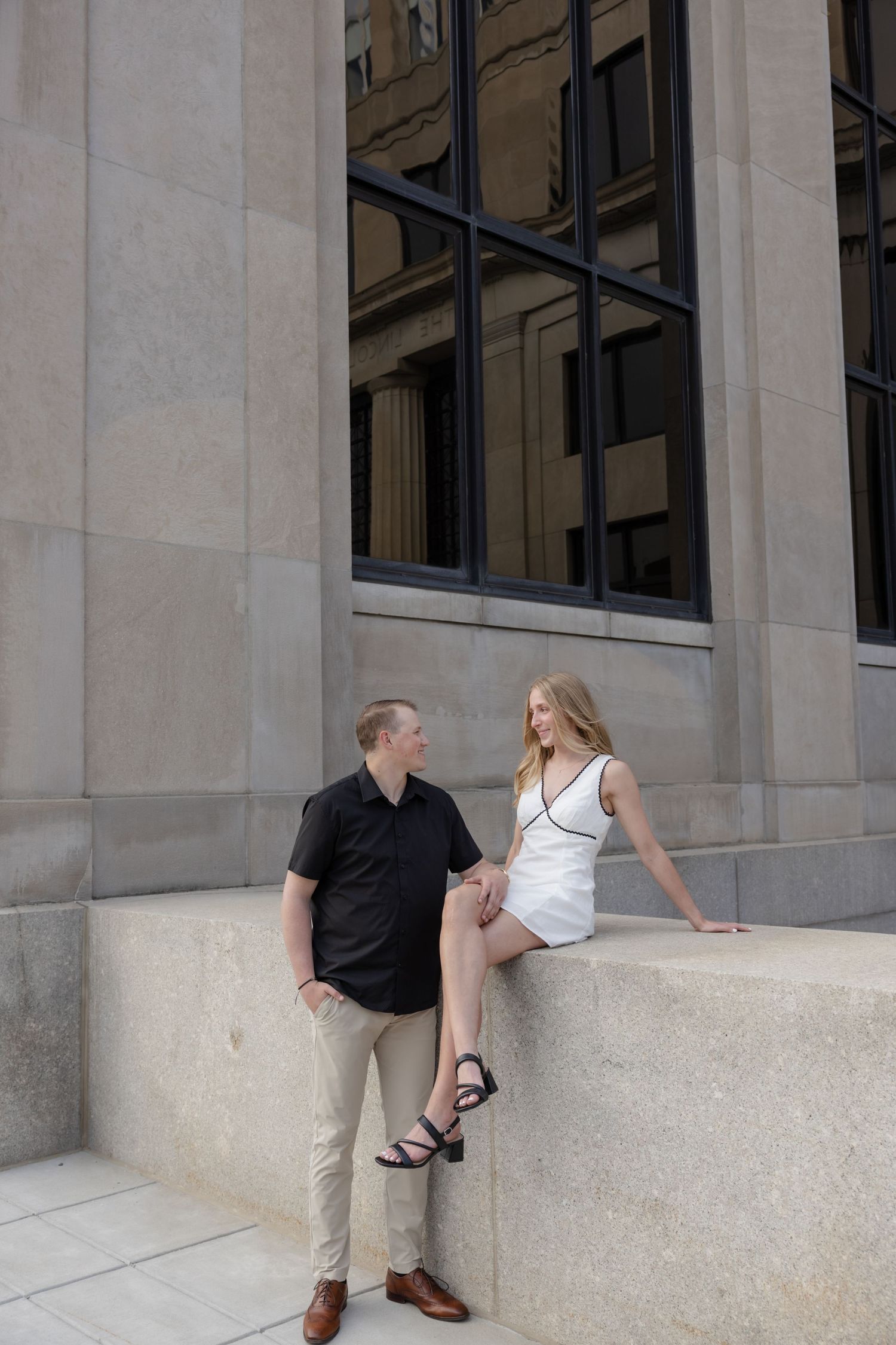 Two people posing together against a white stone building exterior.