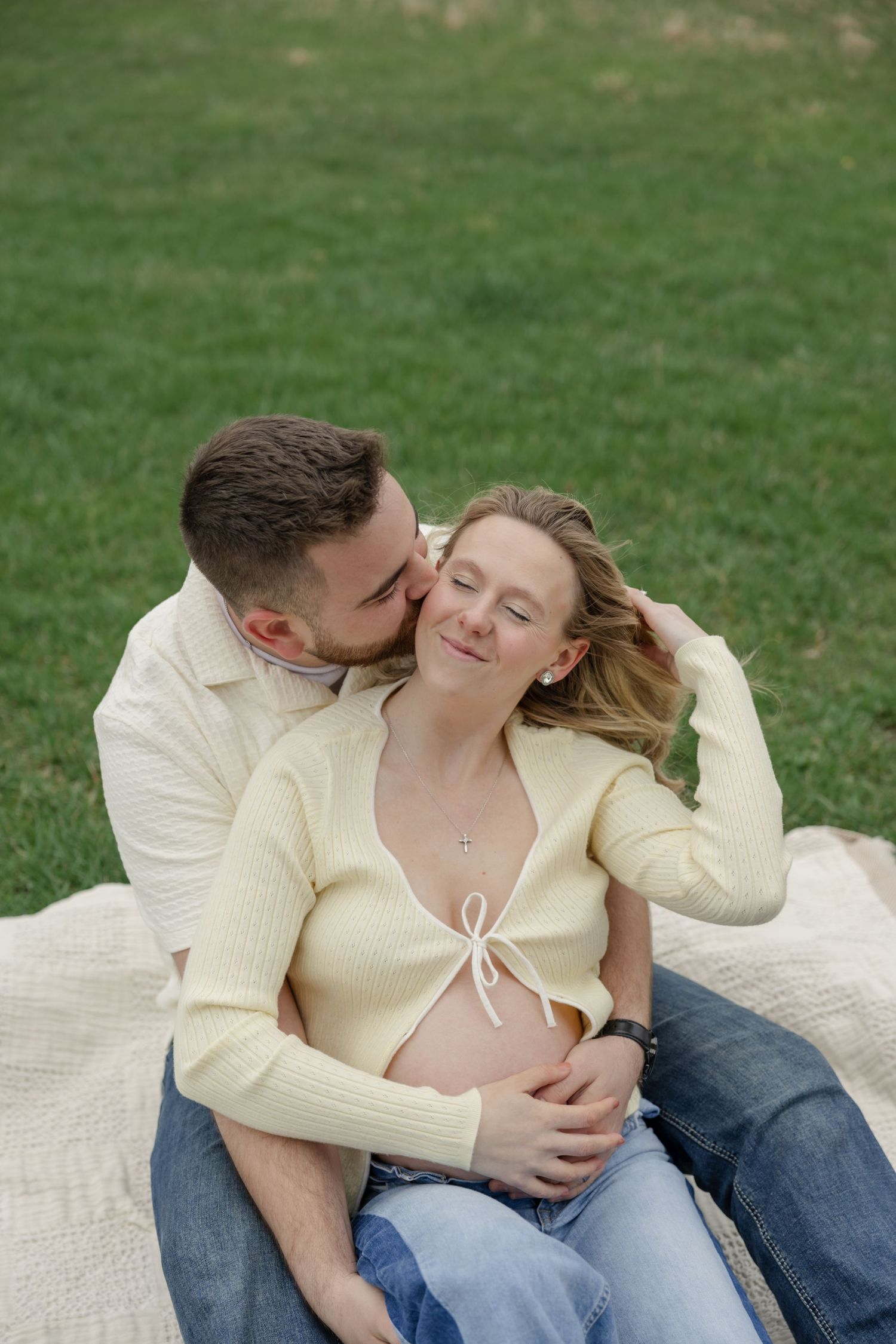 Intimate maternity photo of couple sitting together on blanket outdoors.