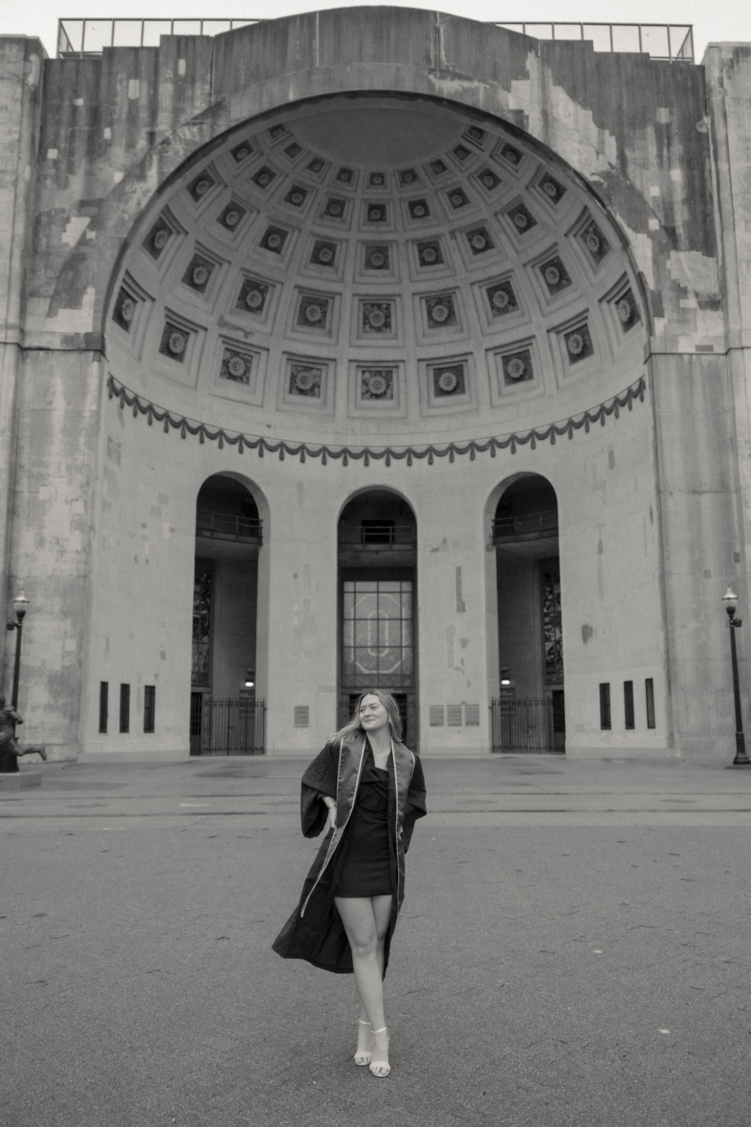 A figure poses in front of an ornate domed building entrance with classical architectural details in black and white.