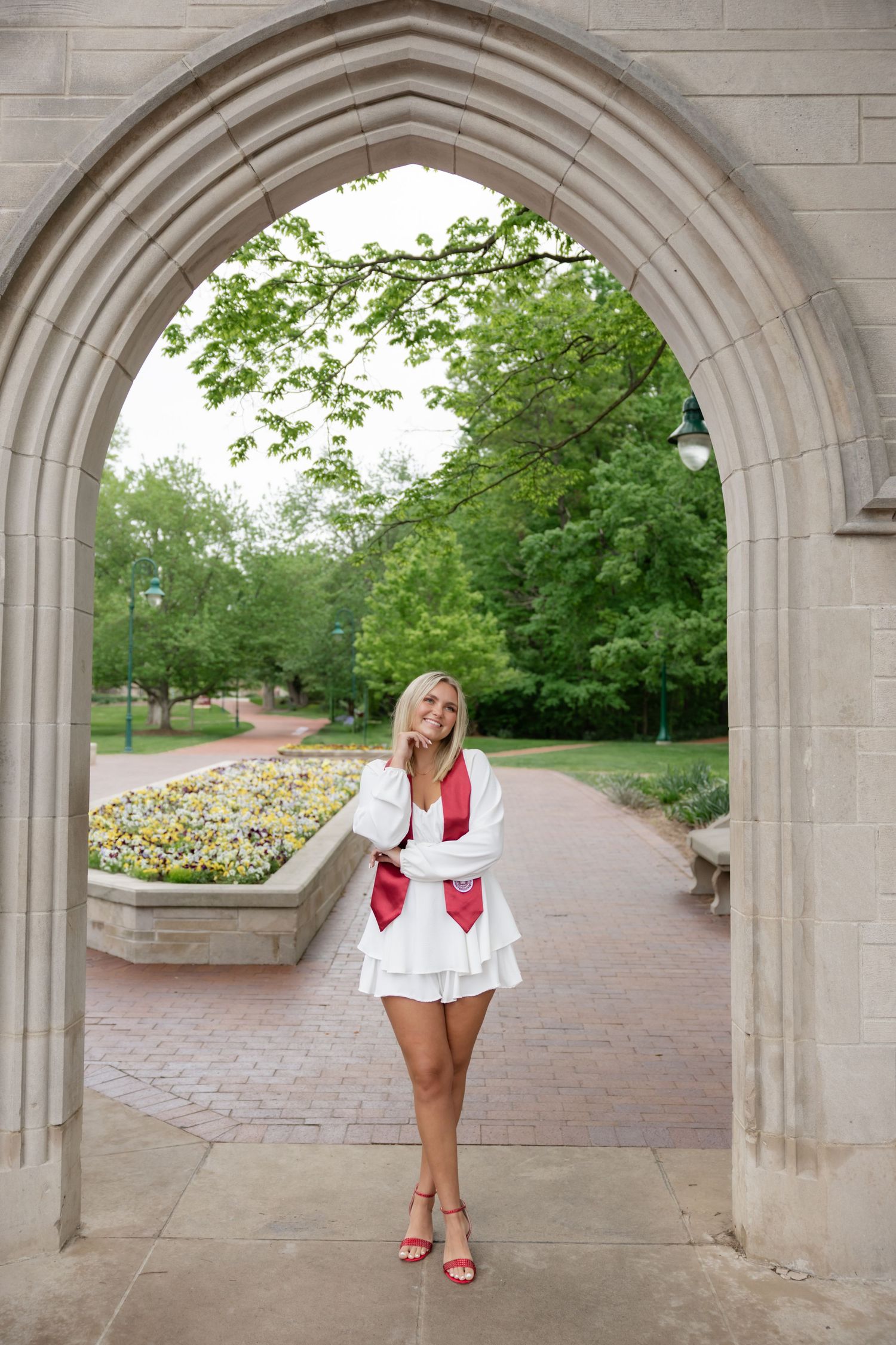 Gothic stone archway frames a brick pathway with flowering garden beds on campus.