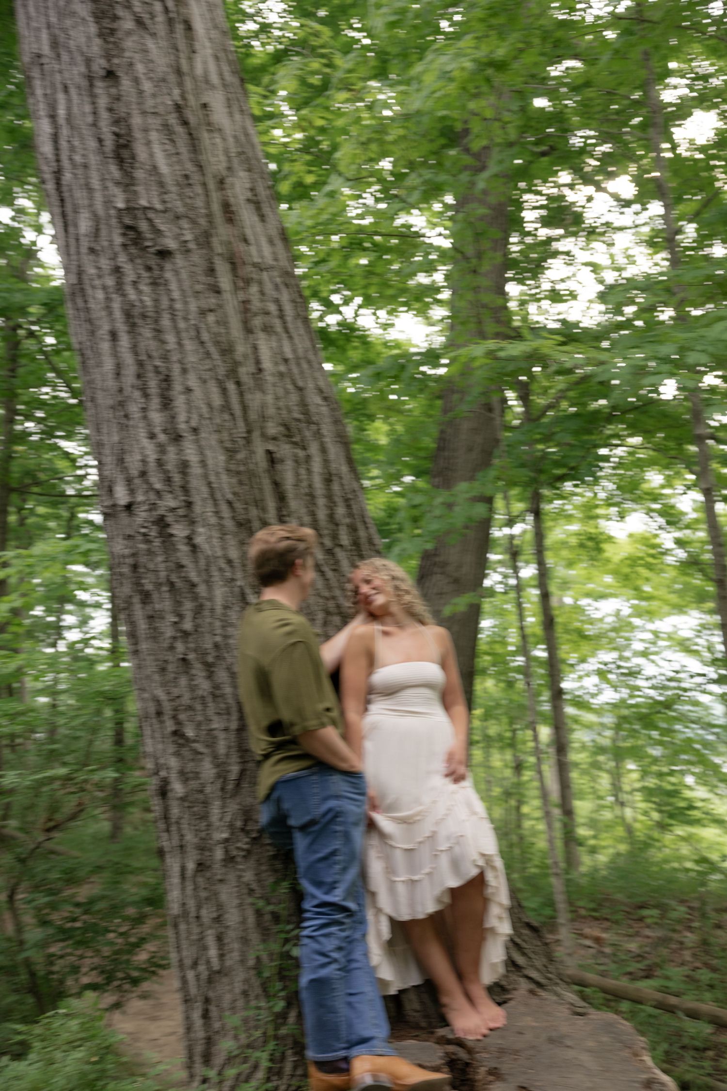 Romantic moment captured between couple near large tree trunks in wooded setting.