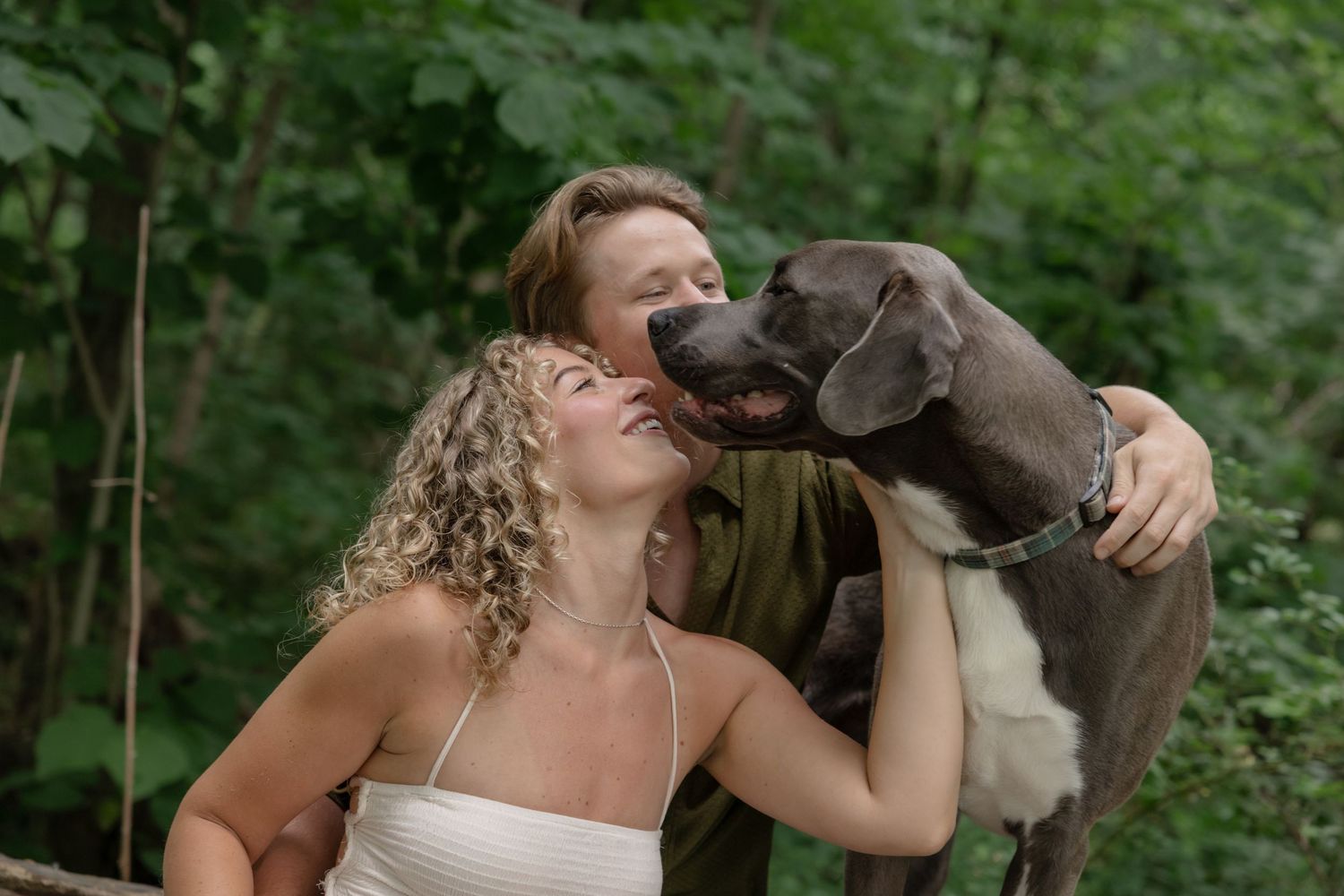 Person in white dress laughing while interacting with a brown dog outdoors.