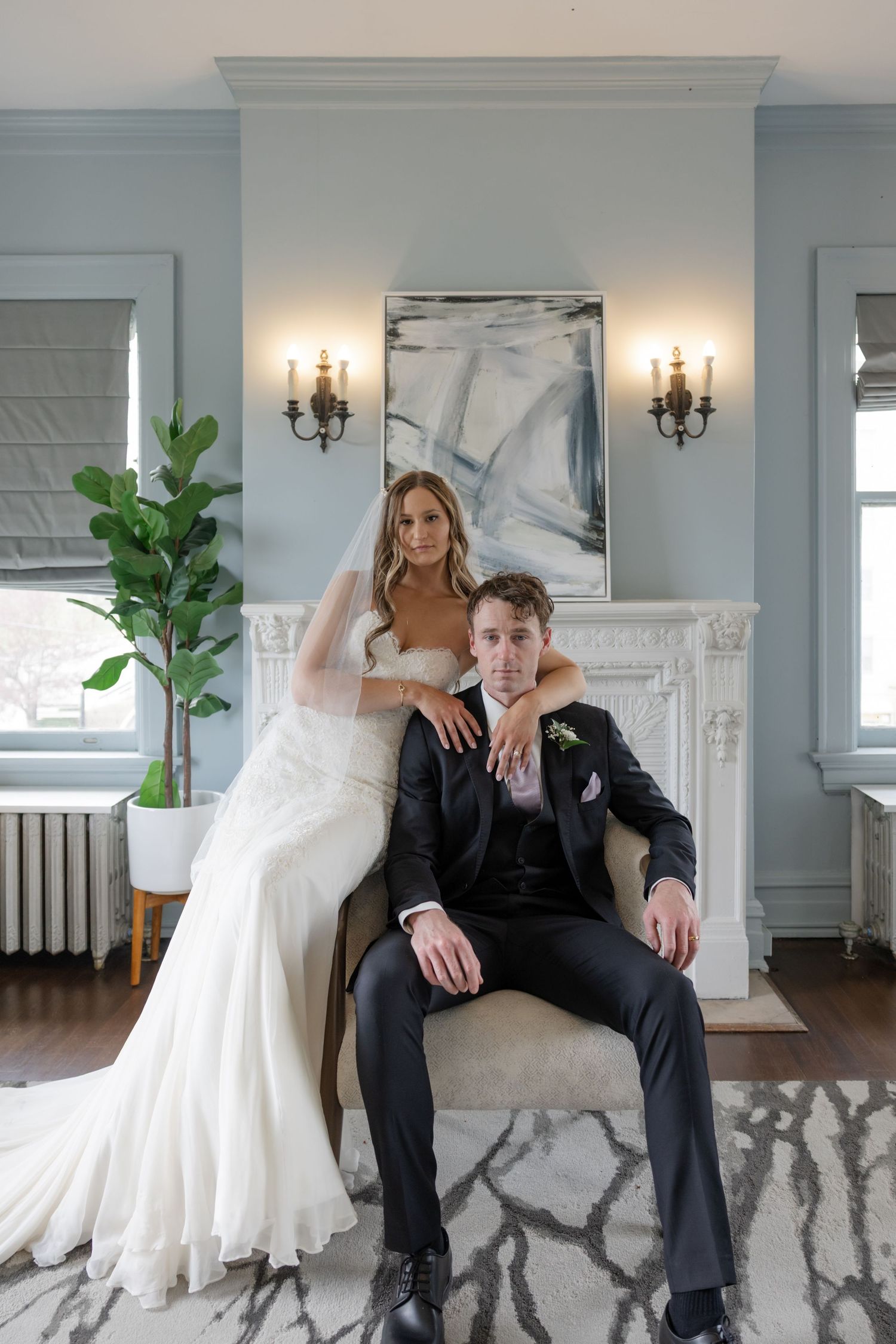 Elegant wedding couple poses in modern interior with marble fireplace and fiddle leaf fig plant.