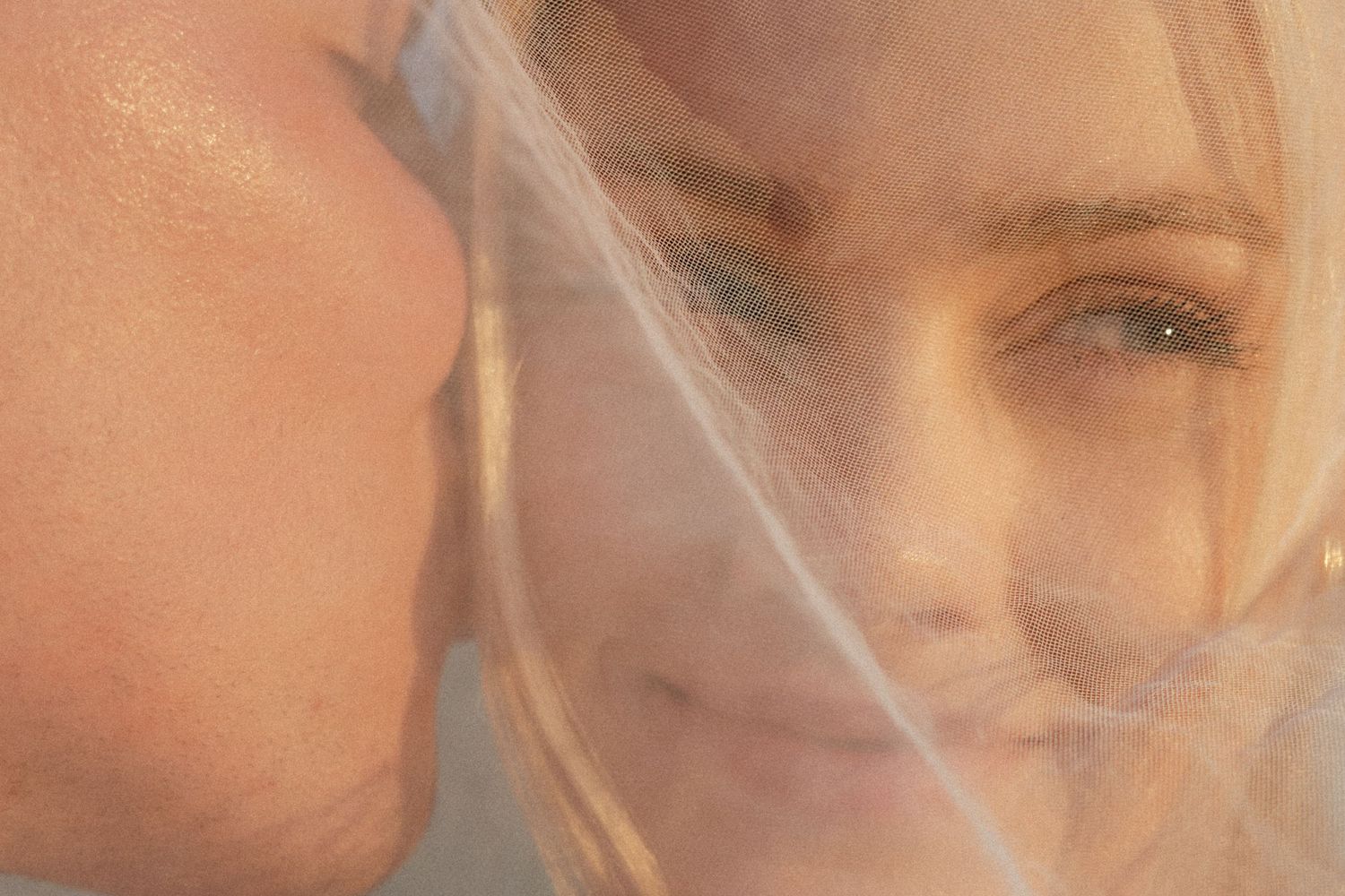 Close-up detail shot of a romantic couple through sheer wedding veil fabric.