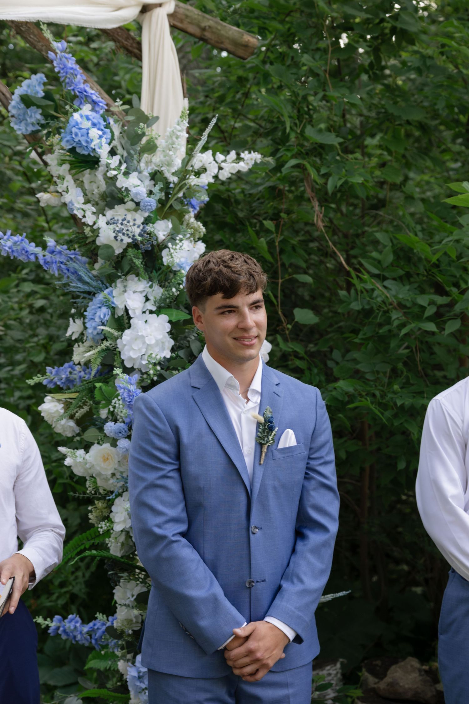 Wedding party members posed with white and blue floral decorations outdoors.