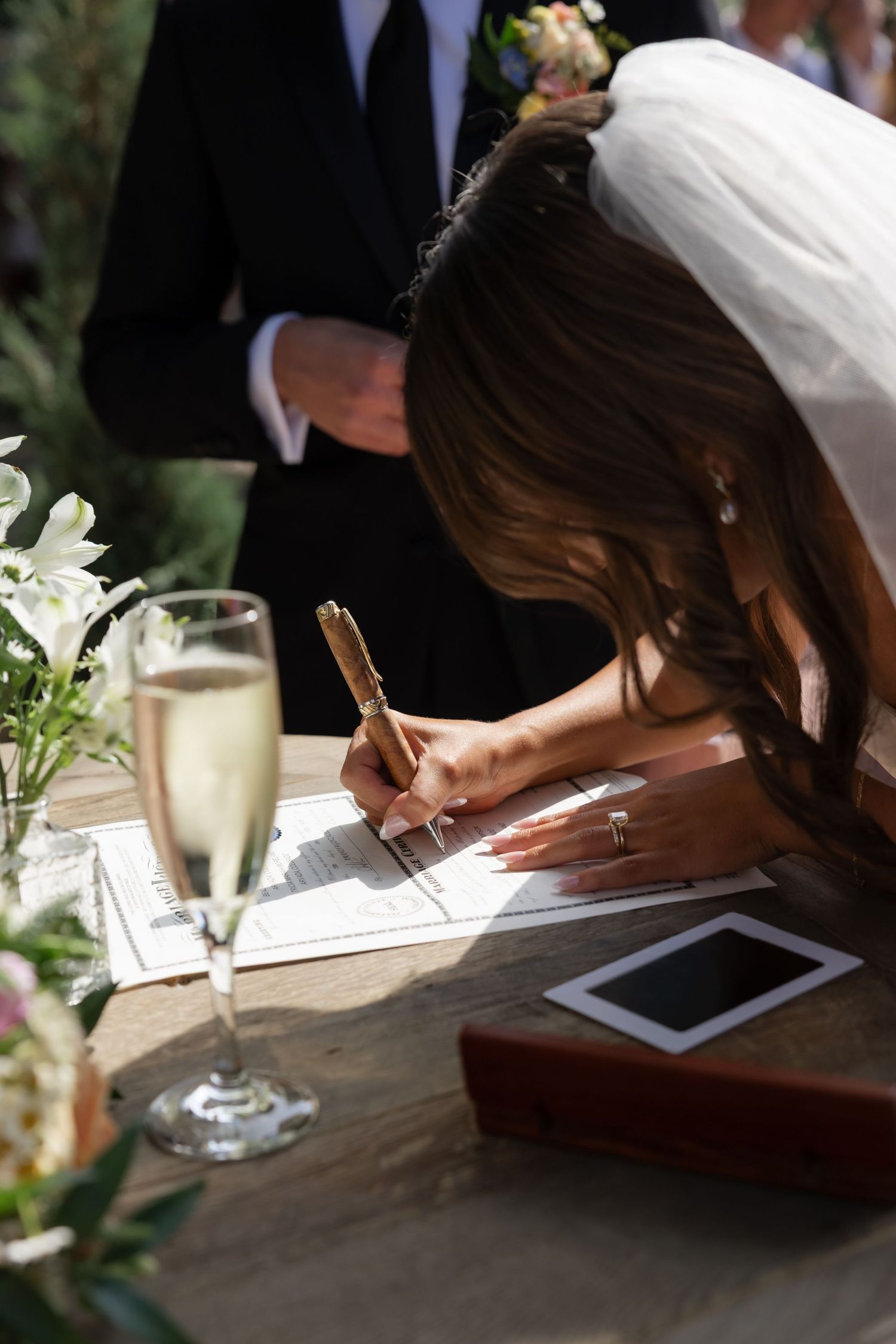 A wedding scene with champagne and document signing at an outdoor reception.