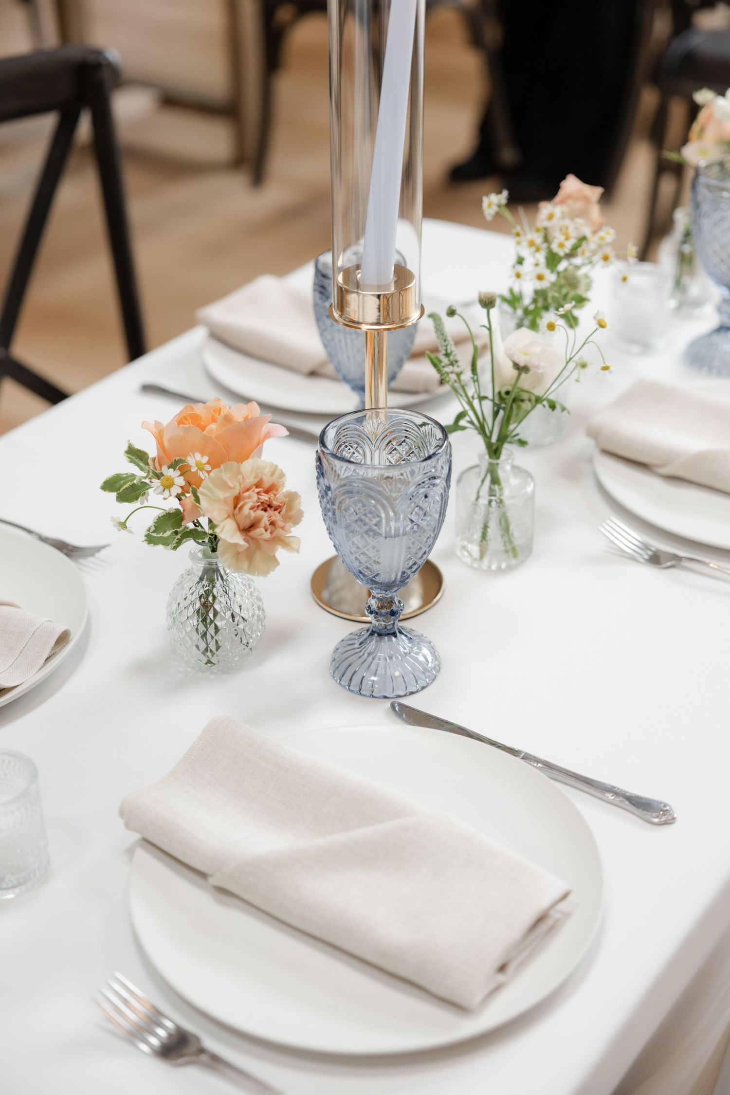 Elegant table setting with delicate floral arrangements, blue glassware, and white napkins.