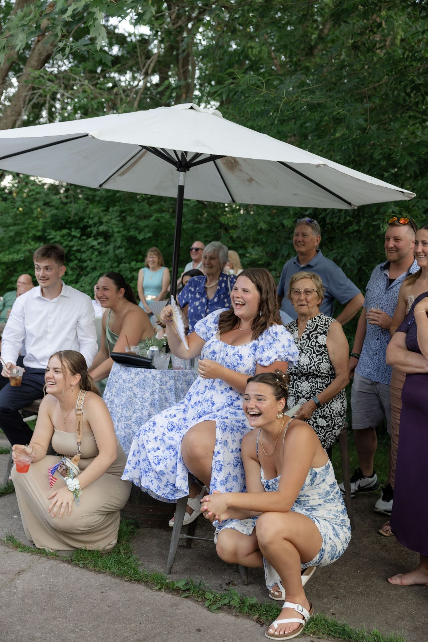 Wedding guests laughing and enjoying themselves under white umbrellas at outdoor reception.