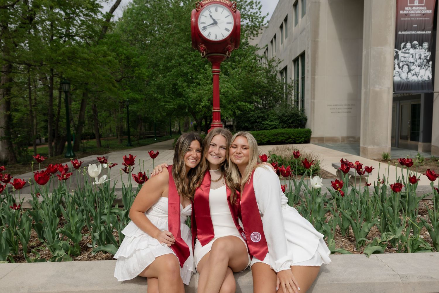 A scenic campus courtyard features blooming red tulips and a prominent circular clock mounted on a decorative pole.