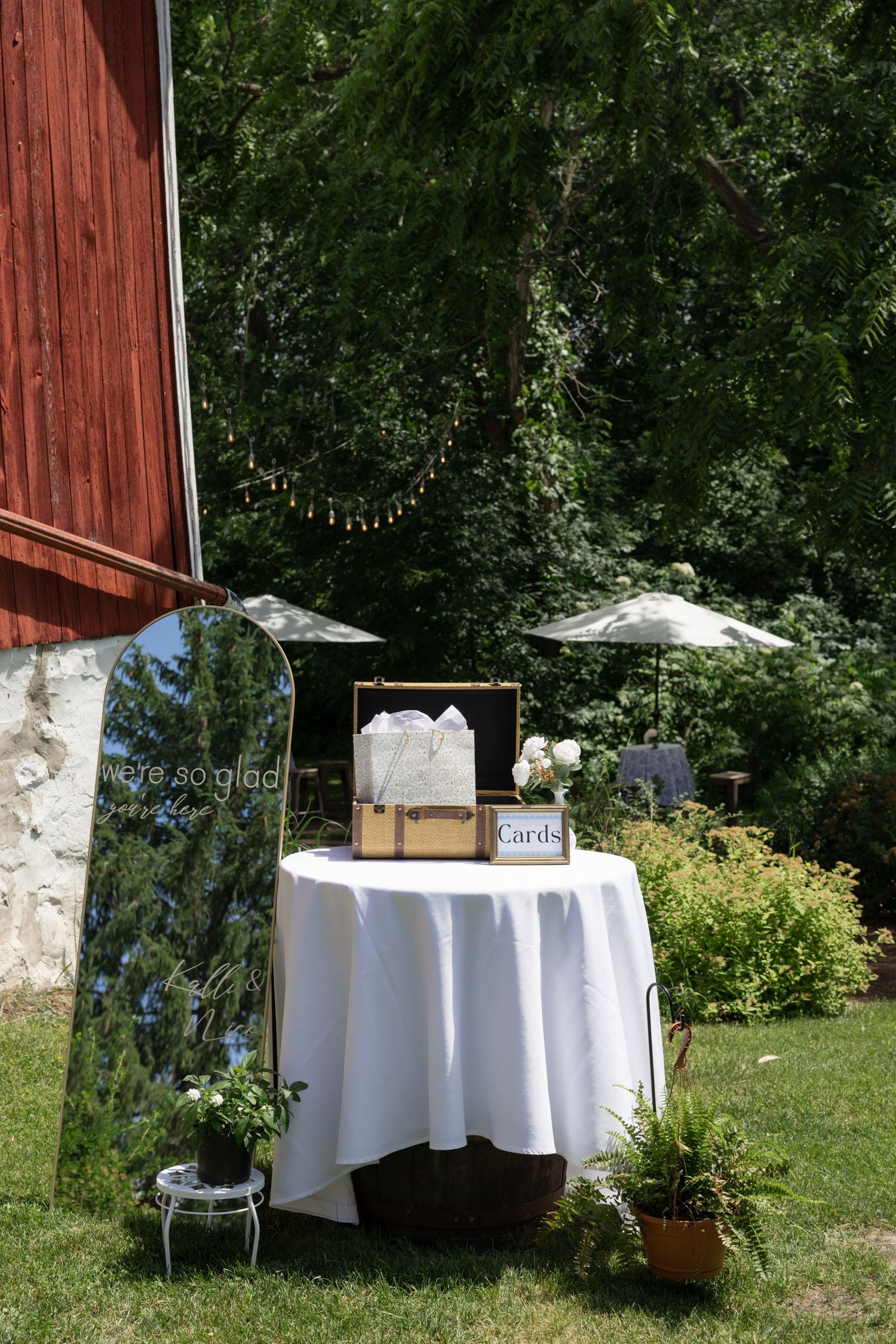 White reception tables set up outdoors near rustic red barn wall.