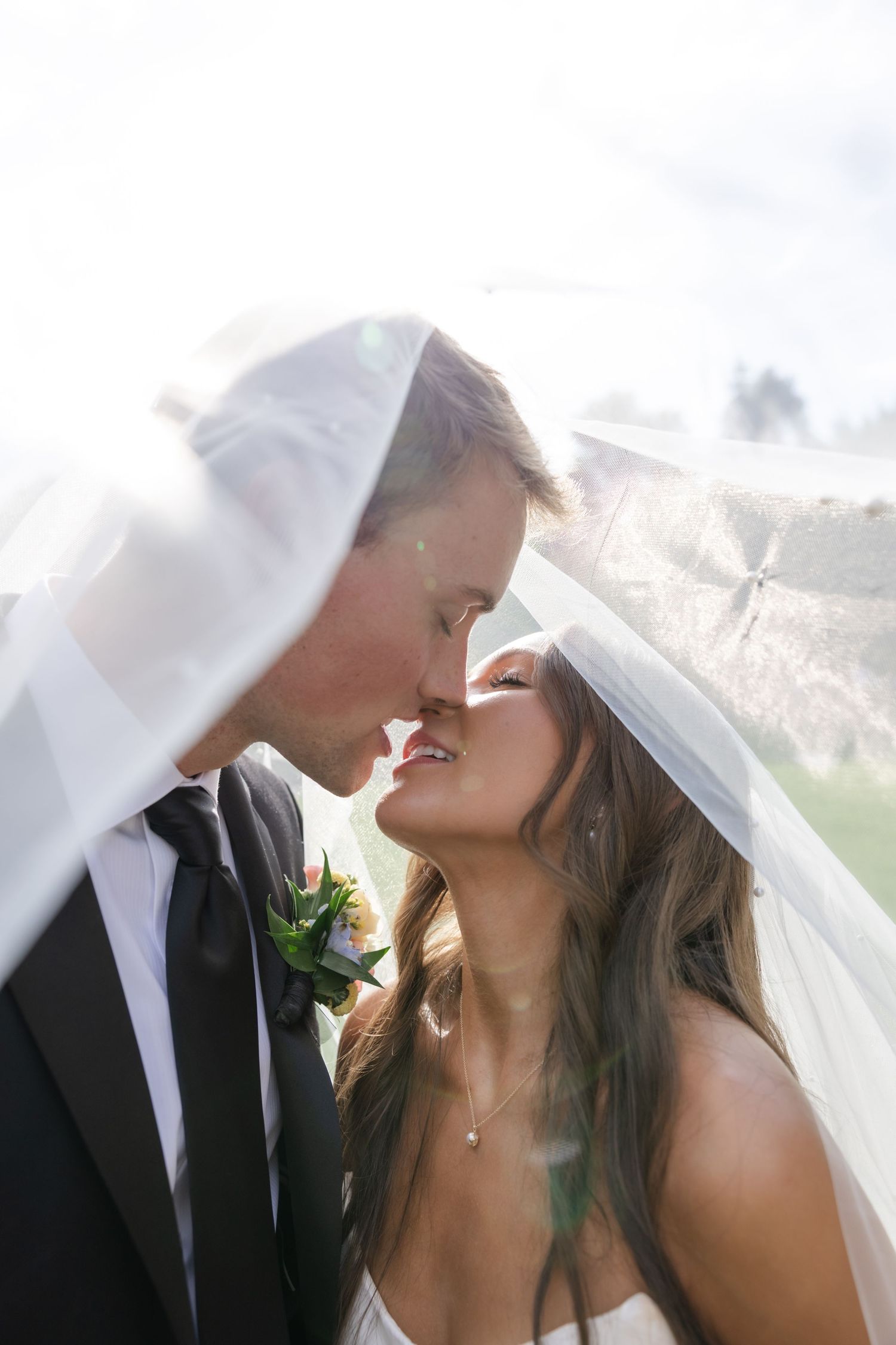 Intimate wedding couple shares romantic moment under flowing white veil.