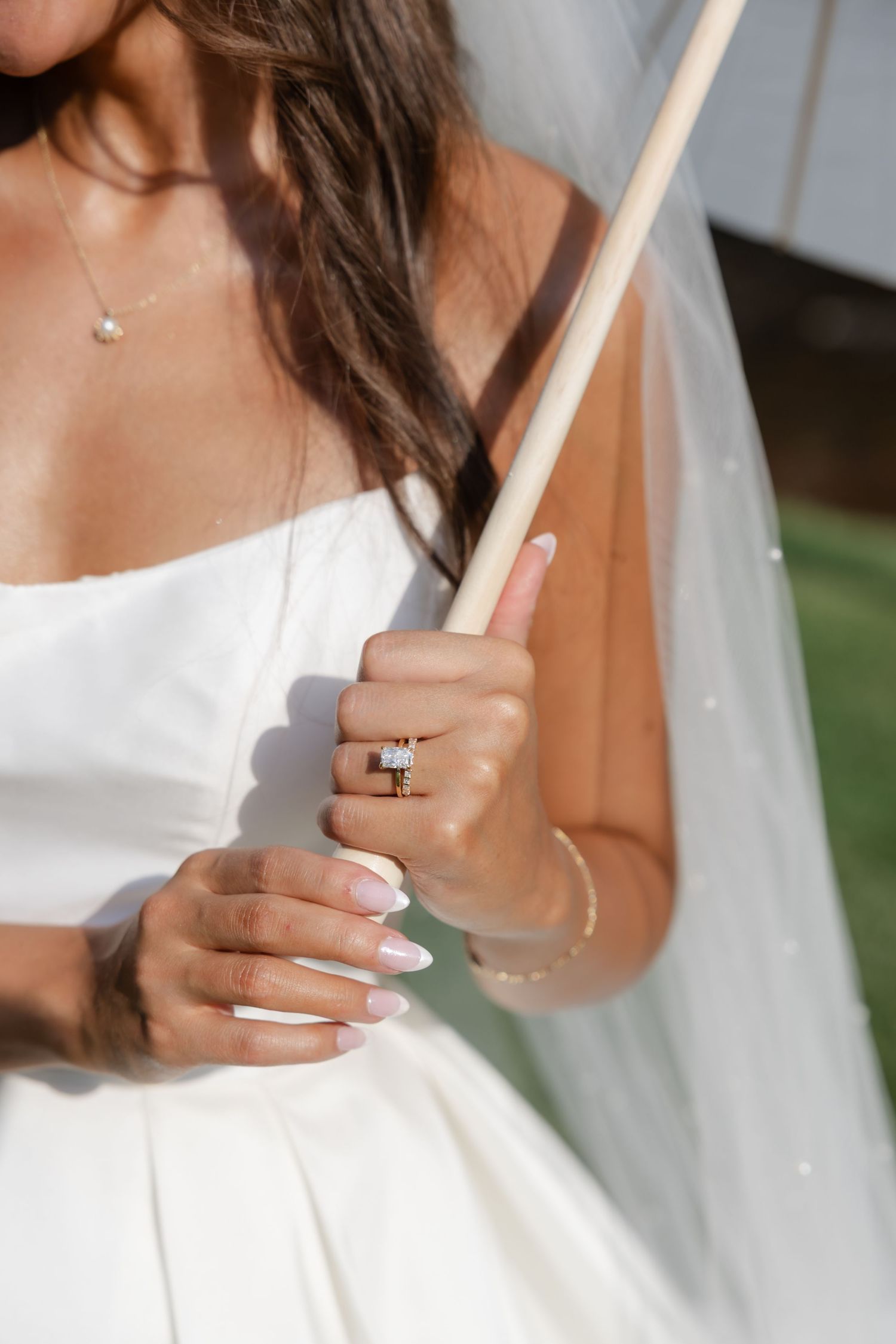 Close-up of bride's hands holding parasol handle showing engagement ring and white manicure.