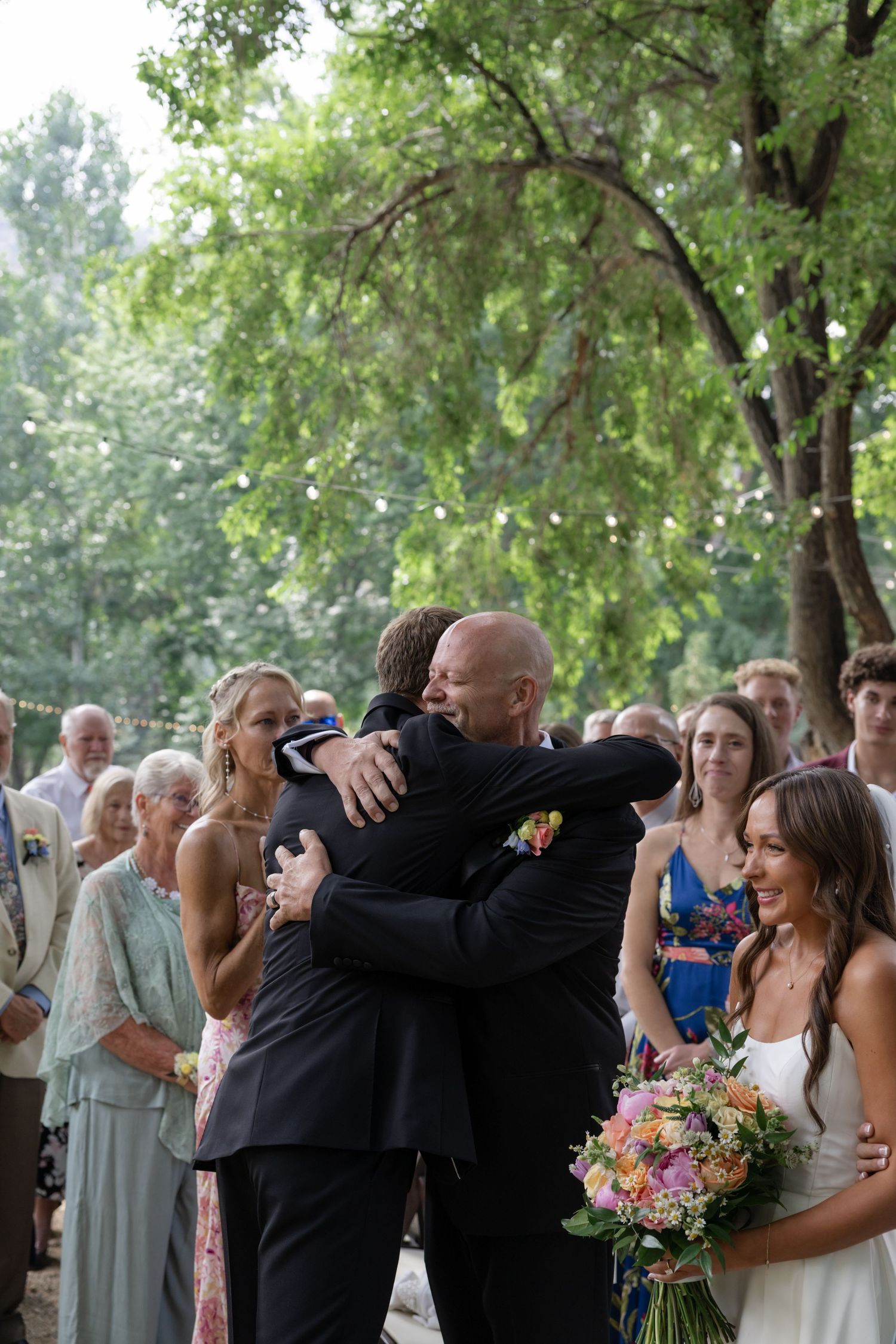 Emotional embrace during outdoor wedding ceremony while guests look on.