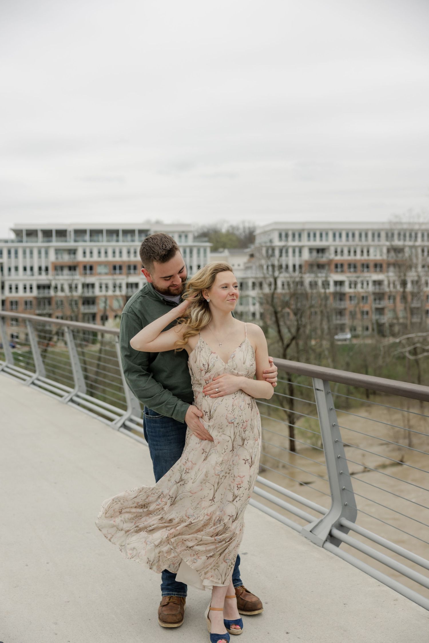Candid moment of couple during maternity photoshoot on a modern bridge structure.