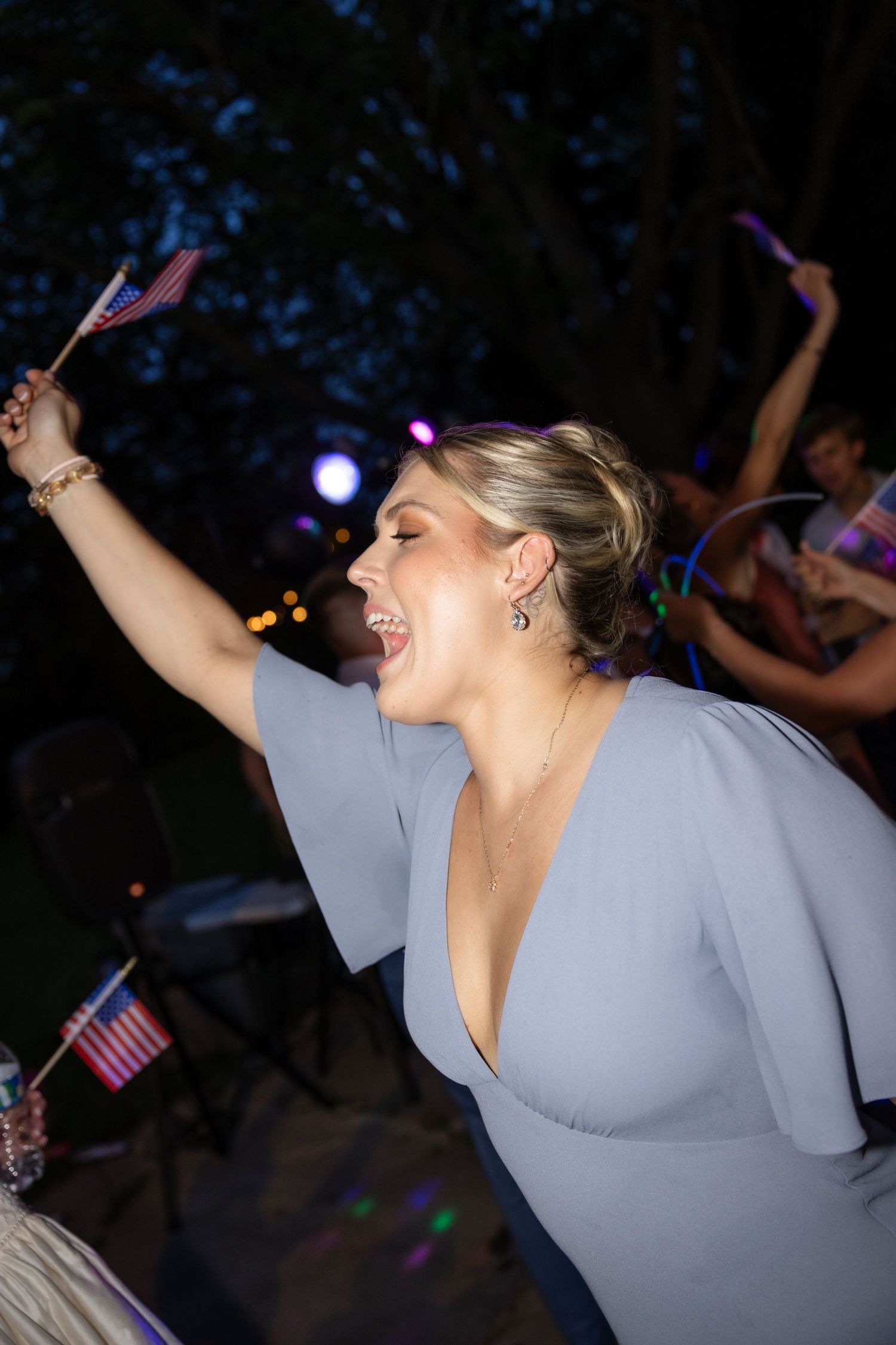 Person in gray dress waves American flag while dancing at outdoor party.