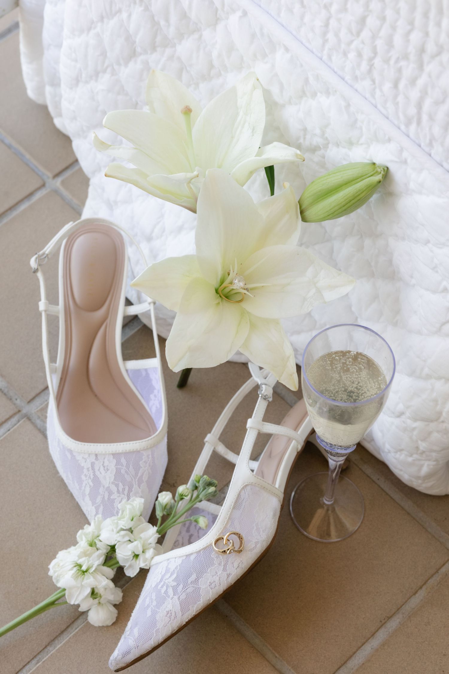 Elegant white bridal shoes with lilies and wedding accessories on display.