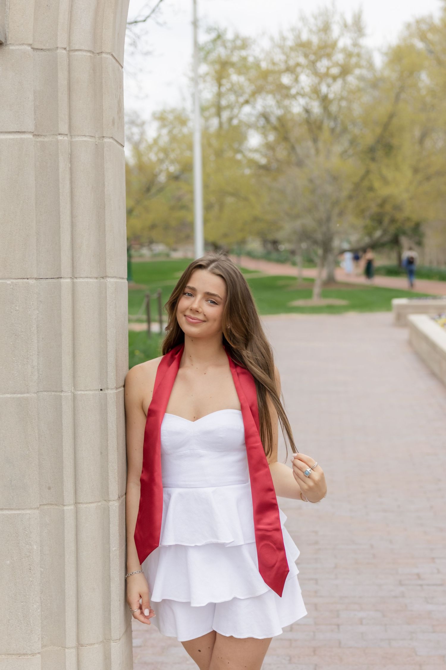 A person in a white summer dress and red stole poses between concrete pillars outdoors.